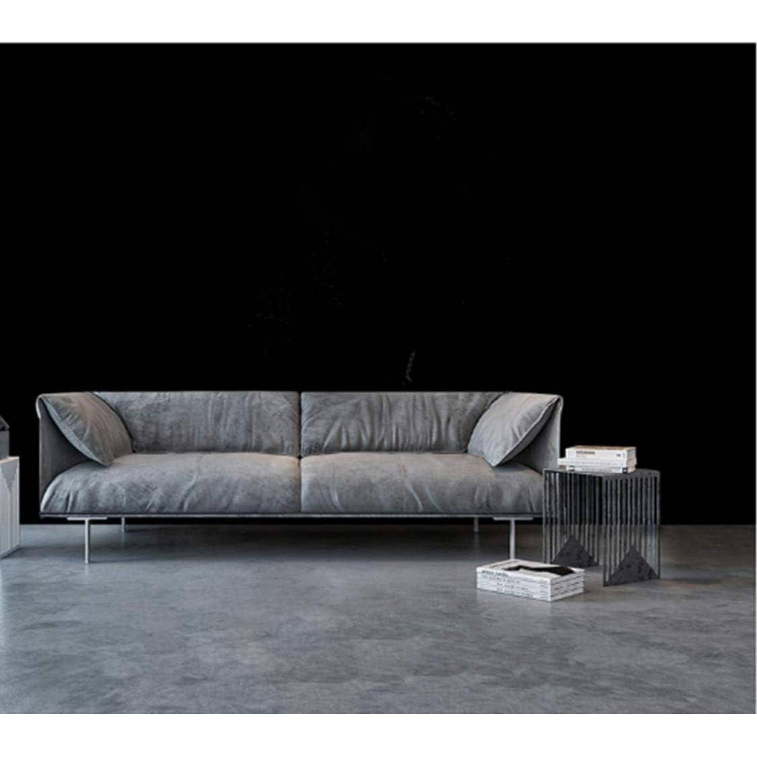 Ein modernes graues Sofa mit Metallfüßen in einem minimalistischen Raum, vor einer schwarzen Wand. Ein geometrischer Beistelltisch und Bücher befinden sich in der Nähe.