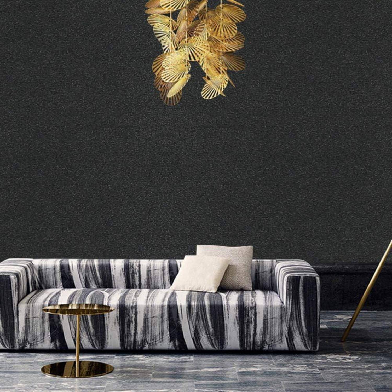 Ein modernes Wohnzimmer mit einem gestreiften Sofa, zwei beigen Kissen, einem kleinen runden Tisch und goldener Wanddekoration auf einer dunklen texturierten Wand.