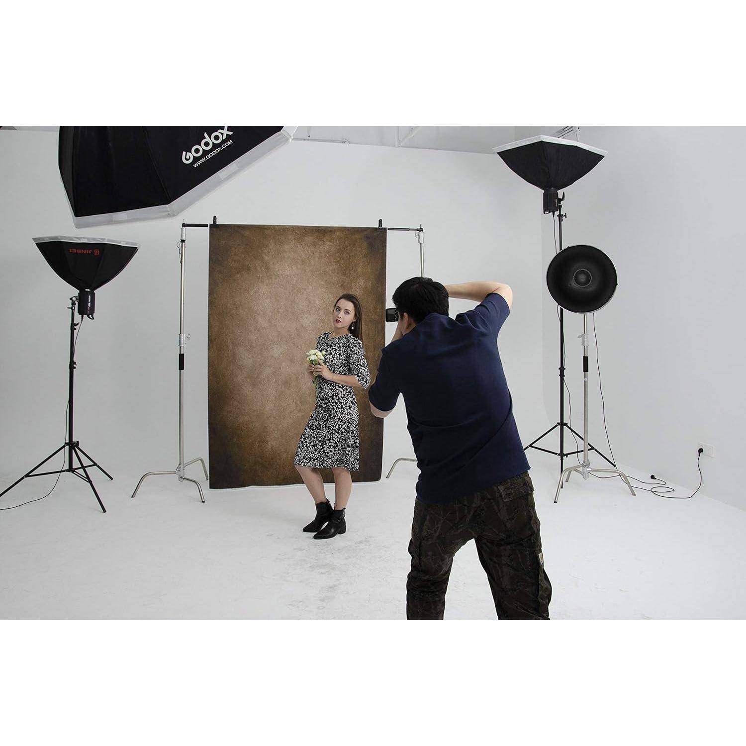 Eine Fotografin lichtet eine stehende Frau in einem Studio mit professioneller Beleuchtungsausrüstung und einem braunen Hintergrund ab.
