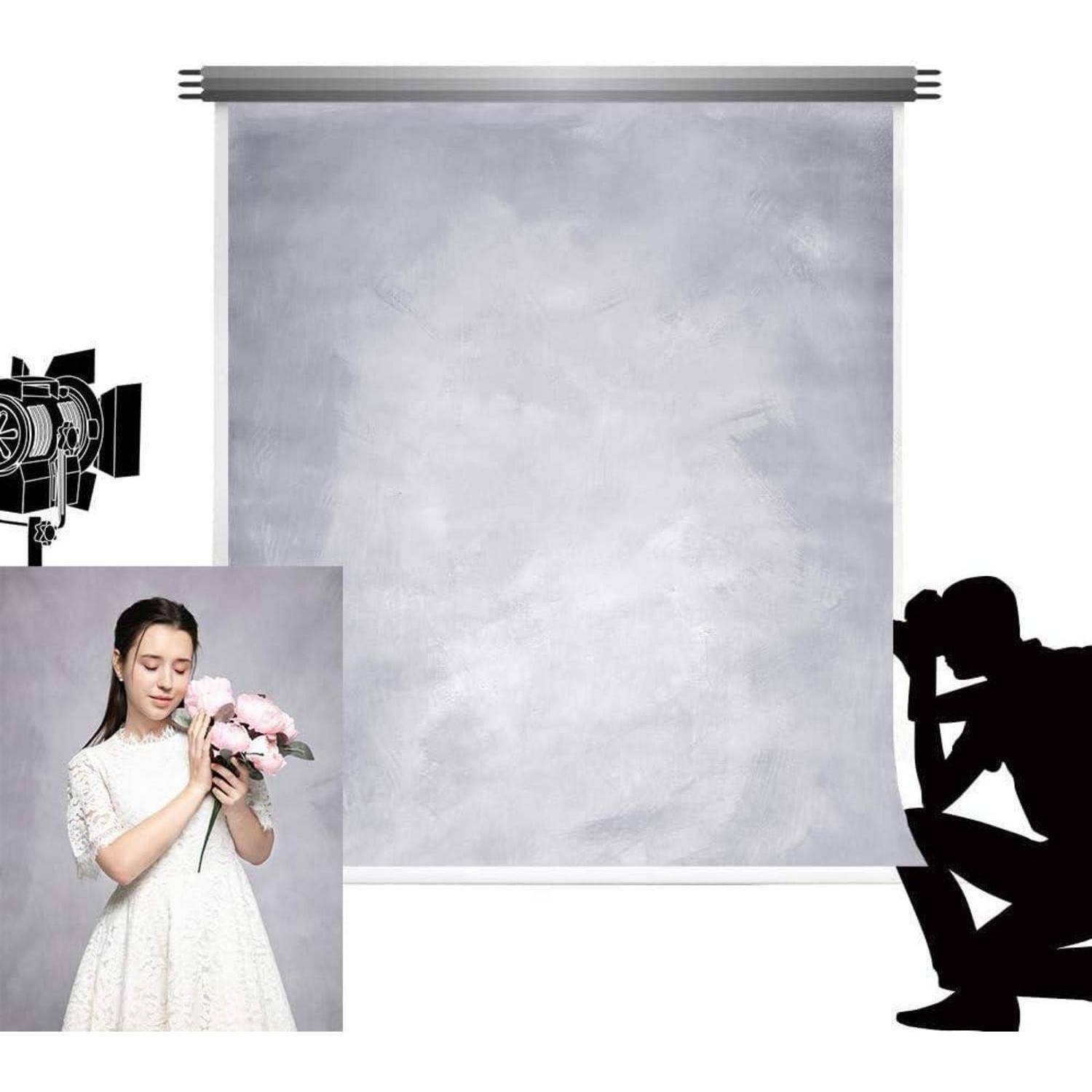 Eine Frau in einem weißen Kleid hält rosa Blumen vor einem grauen Hintergrund in einem Fotostudio. Silhouetten eines Fotografen und der Beleuchtungsausrüstung sind sichtbar.