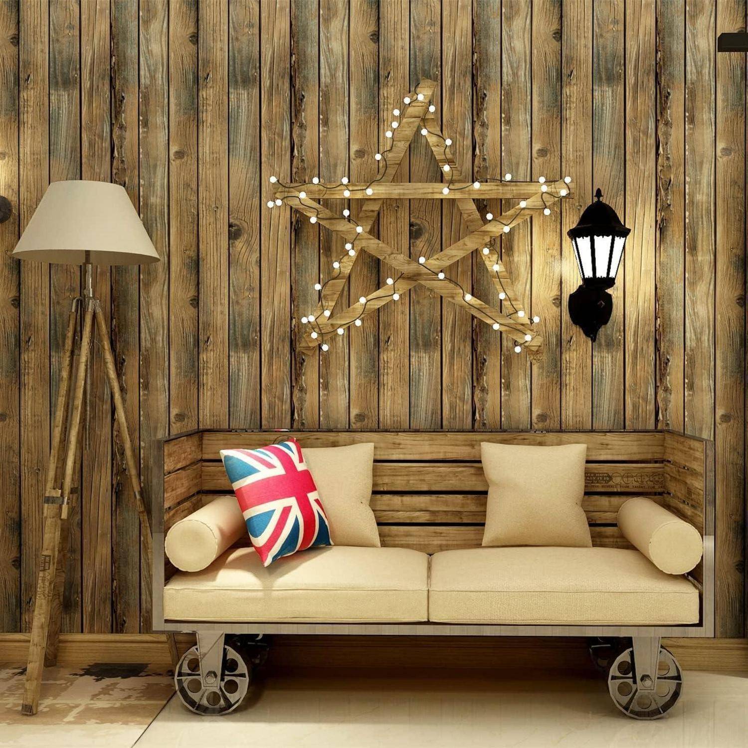 Ein rustikaler Raum zeigt eine Holzwand mit sternförmigen Lichterketten, einer Laterne, einer Lampe und einem beigen Sofa mit einem Union Jack Kissen.