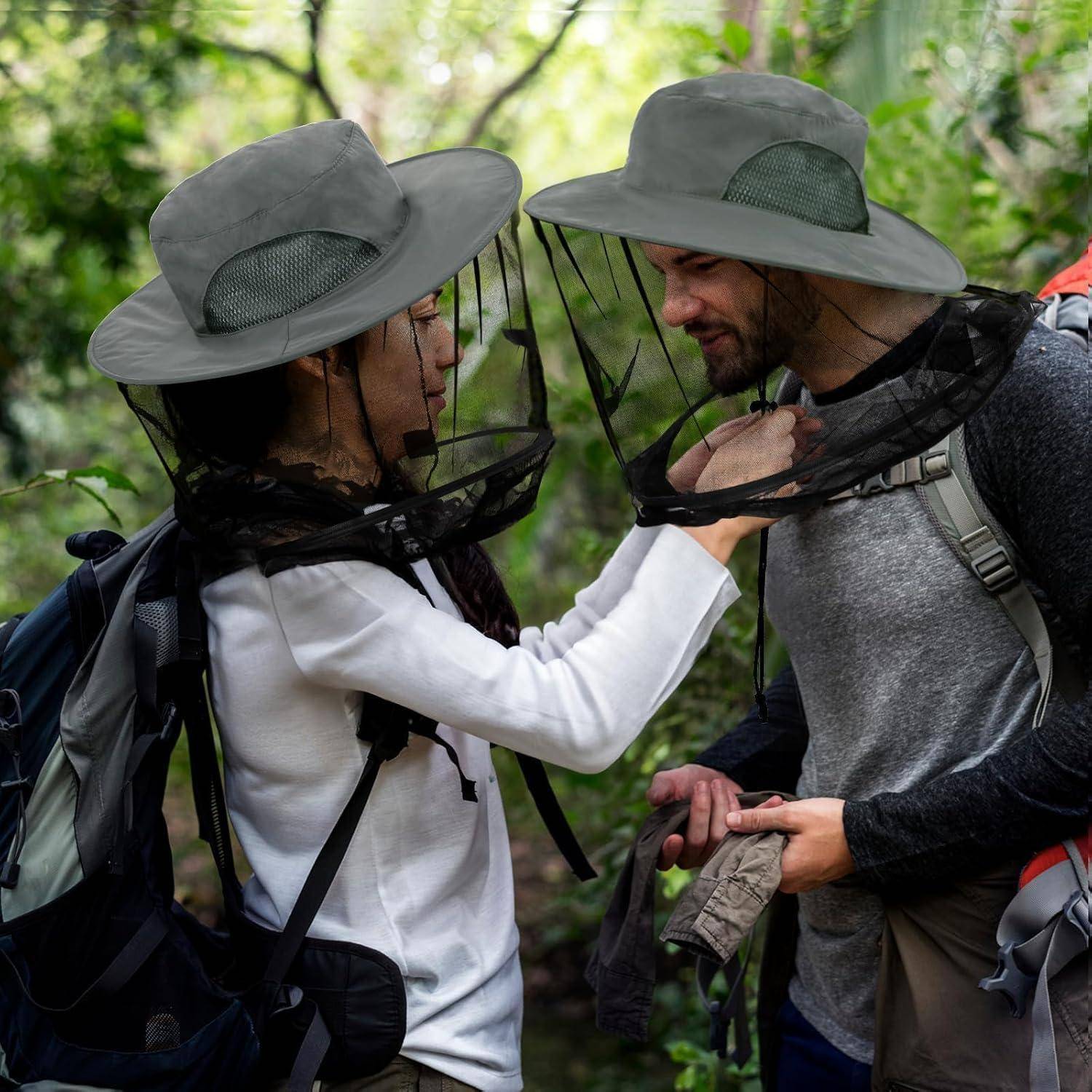 Ein Mann und eine Frau mit Hüten, die mit Moskitonetzen versehen sind, lächeln sich inmitten üppiger Vegetation an und tragen Rucksäcke, was auf einen Wanderausflug hindeutet.