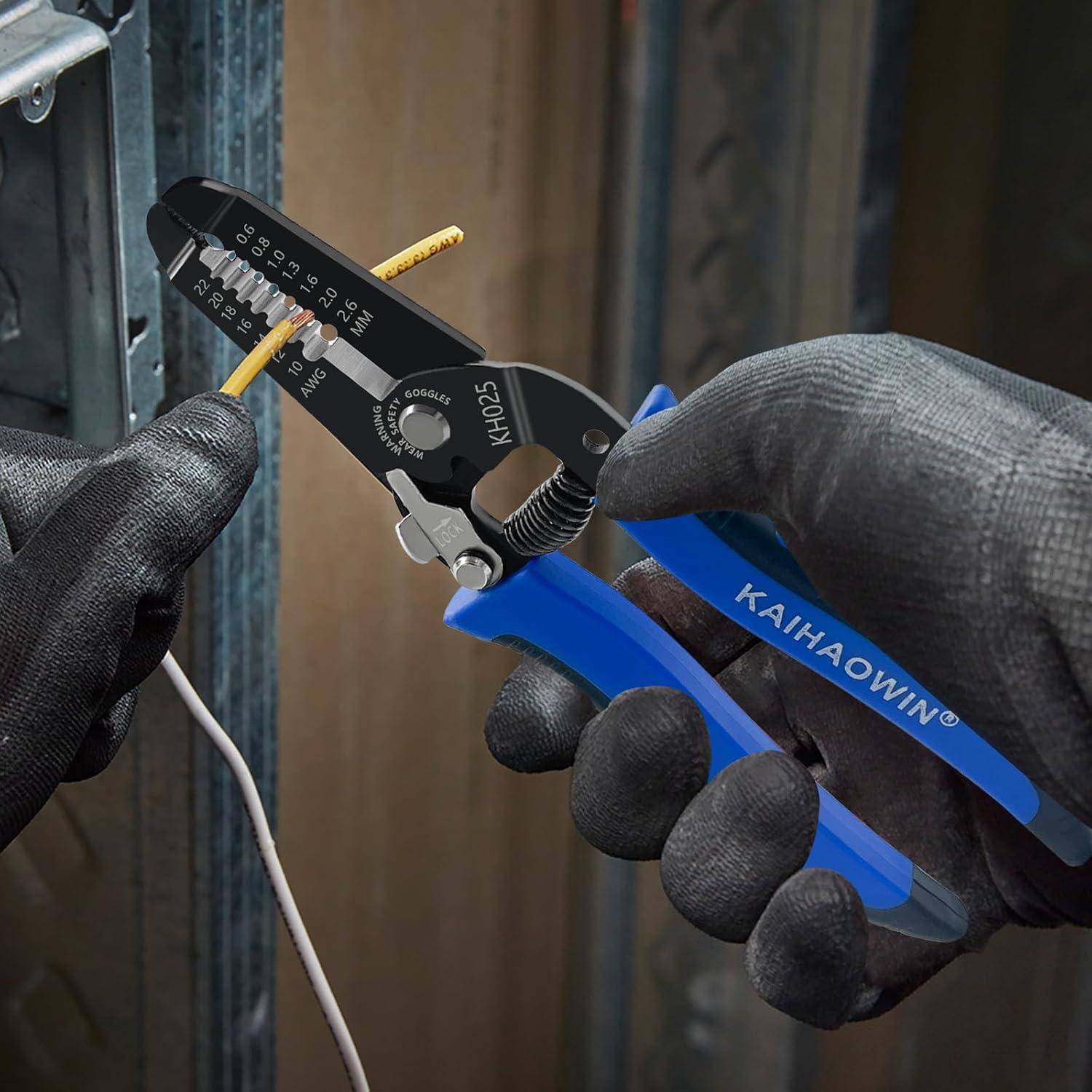 Eine Person trägt schwarze Handschuhe und verwendet eine Abisolierzange mit blauem Griff, um ein weißes Elektrokabel vor einem Metallgehäuse abzuschneiden oder abzuisolieren.