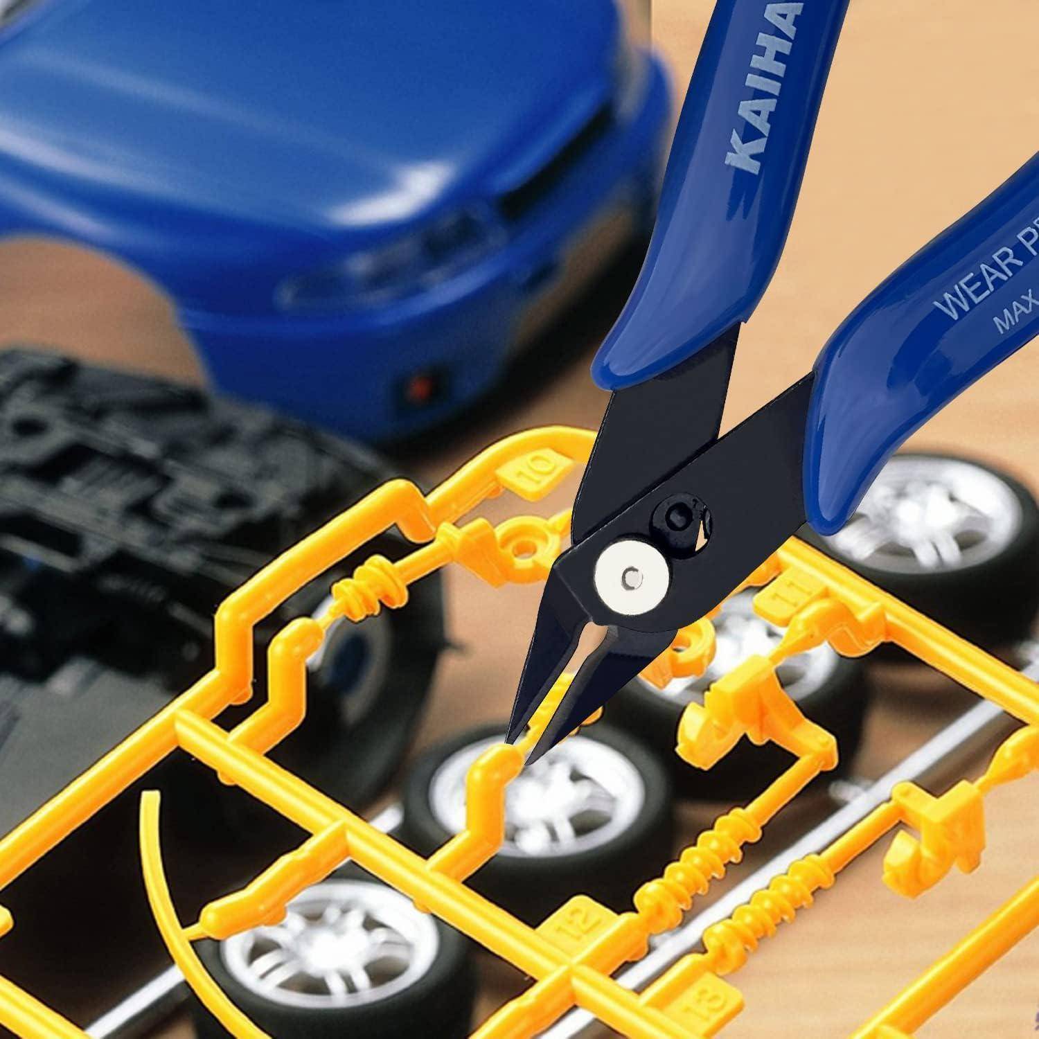 Nahaufnahme von blauen Zangen, die gelbe Plastikteile von einem Modellautobausatz-Anguss abschneiden. Automodellräder und ein blaues Autoteil sind sichtbar.