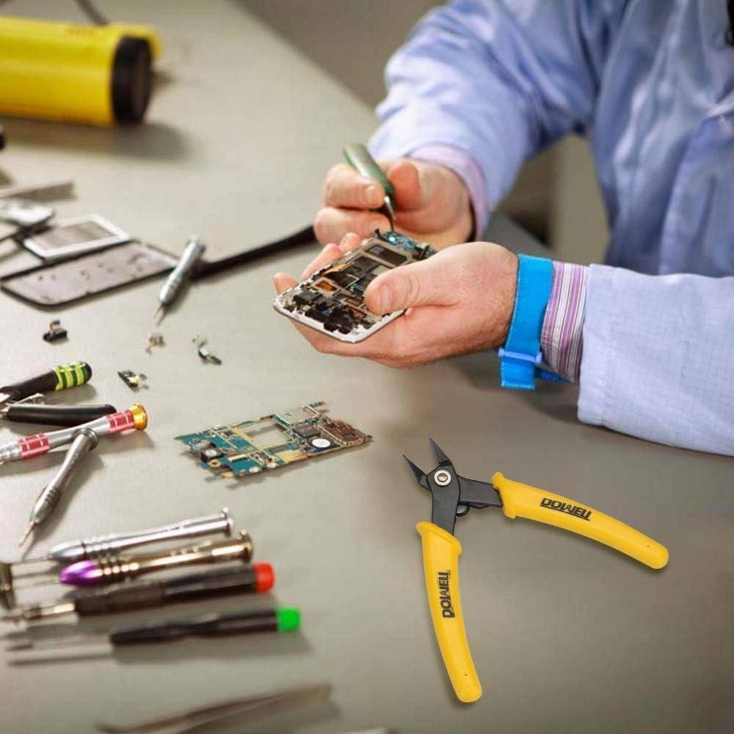 Eine Person repariert ein Smartphone an einem Arbeitstisch, der mit Werkzeugen und Elektronikgeräten übersät ist, darunter Leiterplatten und Zangen.