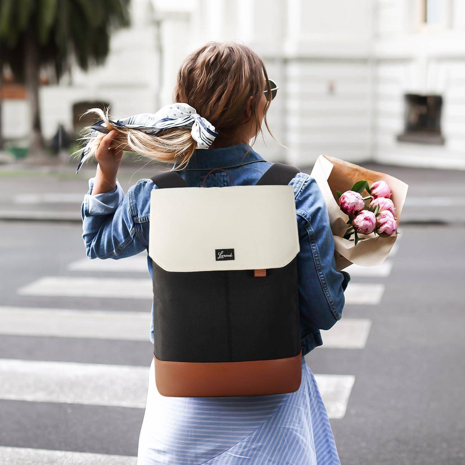 Eine Frau mit einem Rucksack steht an einer Fußgängerampel und hält einen Strauß rosa Blumen. Sie blickt nach rechts, in einer lässigen städtischen Umgebung.
