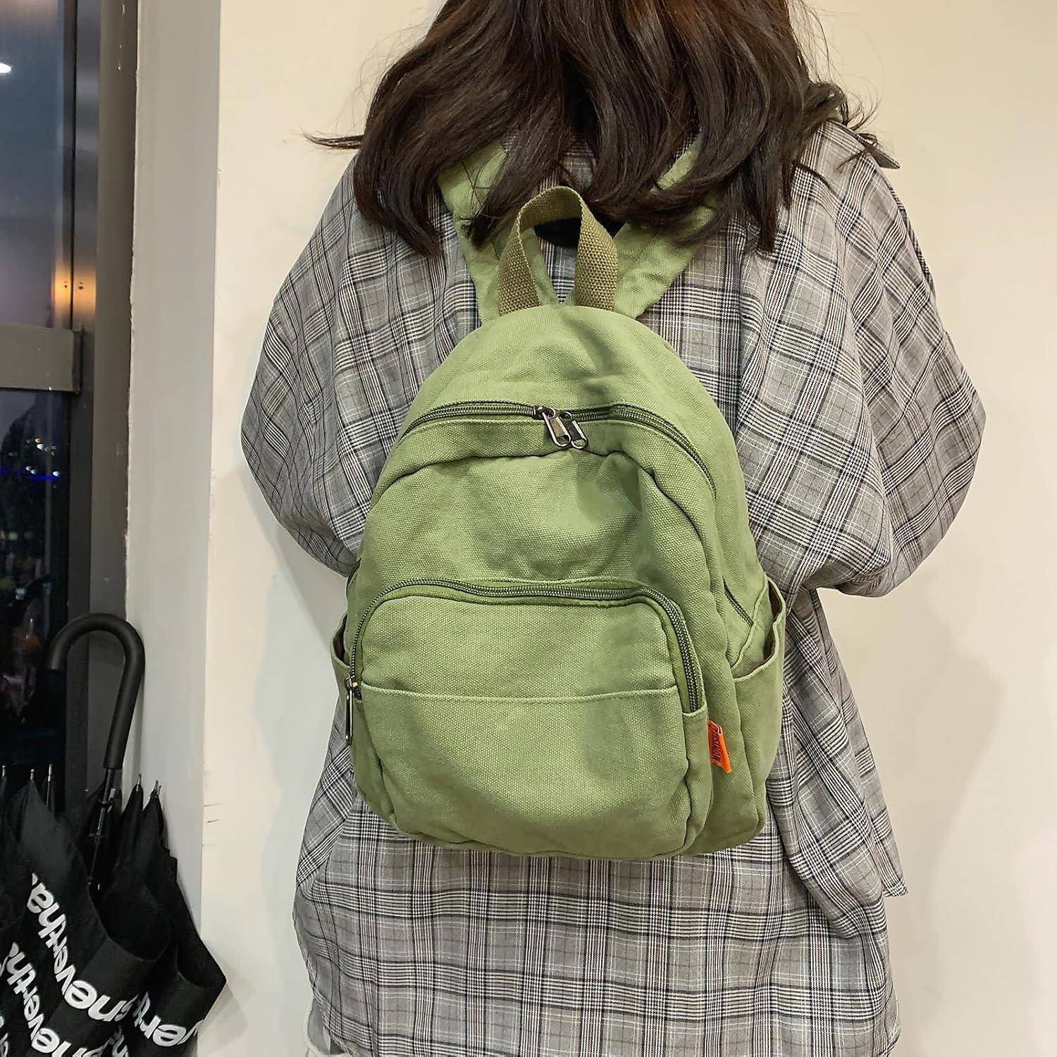 Person von hinten, trägt ein kariertes Hemd und einen grünen Rucksack.