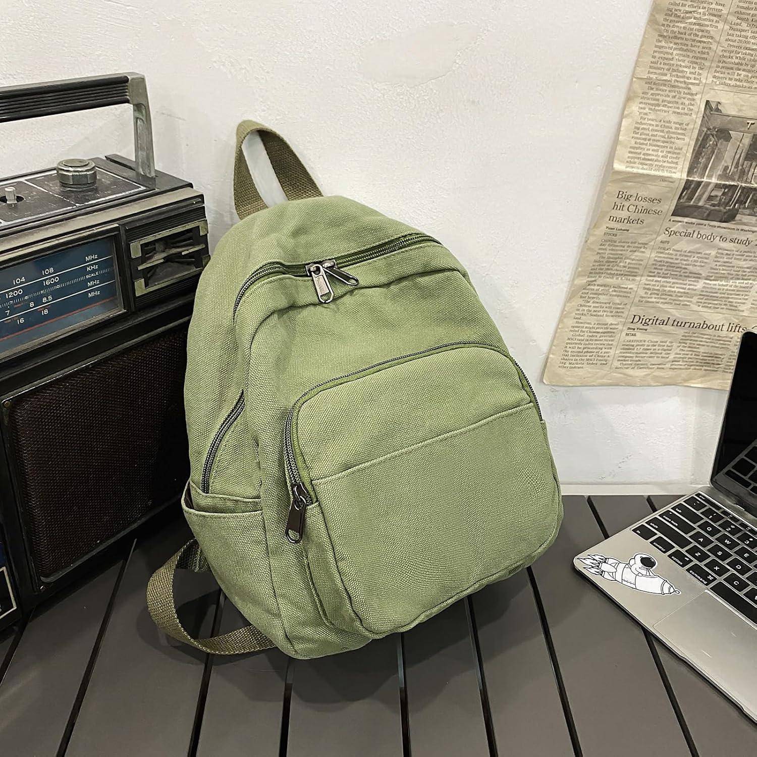 Ein grüner Rucksack auf einem Tisch neben einem Vintage-Radio und einem Laptop, mit einer Zeitung an der Wand im Hintergrund.