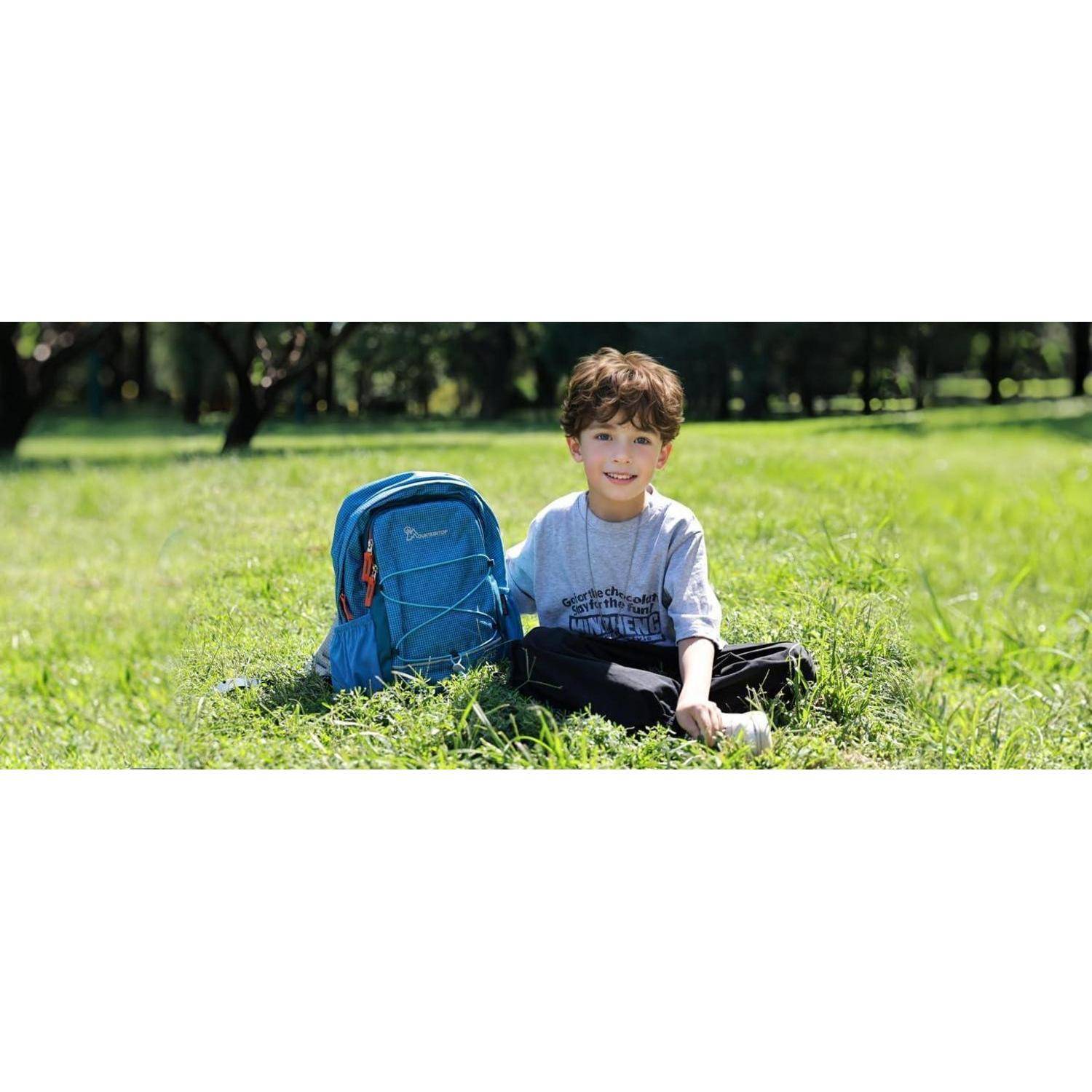 Ein Kind sitzt auf dem Gras in einem Park neben einem blauen Rucksack und lächelt. Bäume und Sonnenlicht sind im Hintergrund sichtbar.