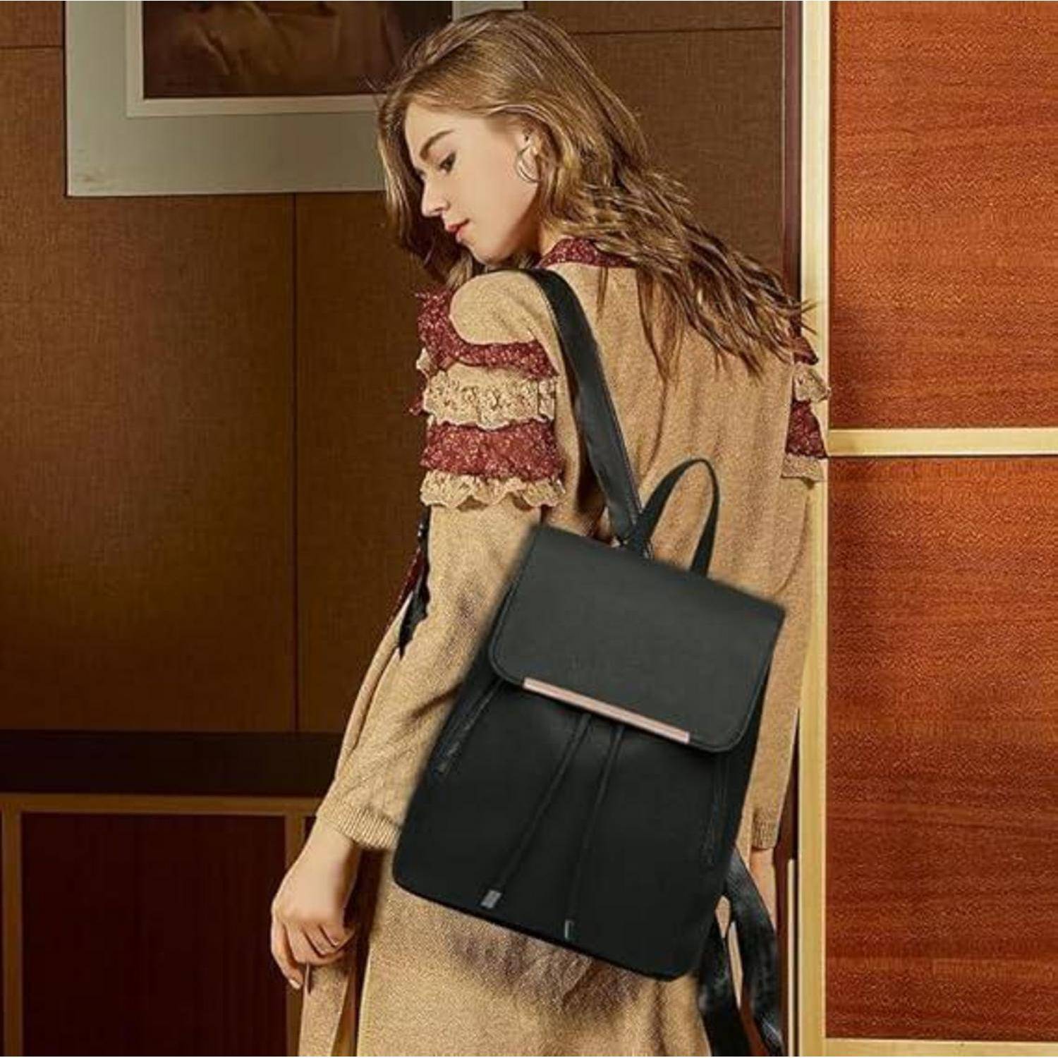 Eine Person mit langen Haaren trägt einen beigen Mantel mit braunen und roten Akzenten, trägt einen schwarzen Lederrucksack und blickt nach unten.