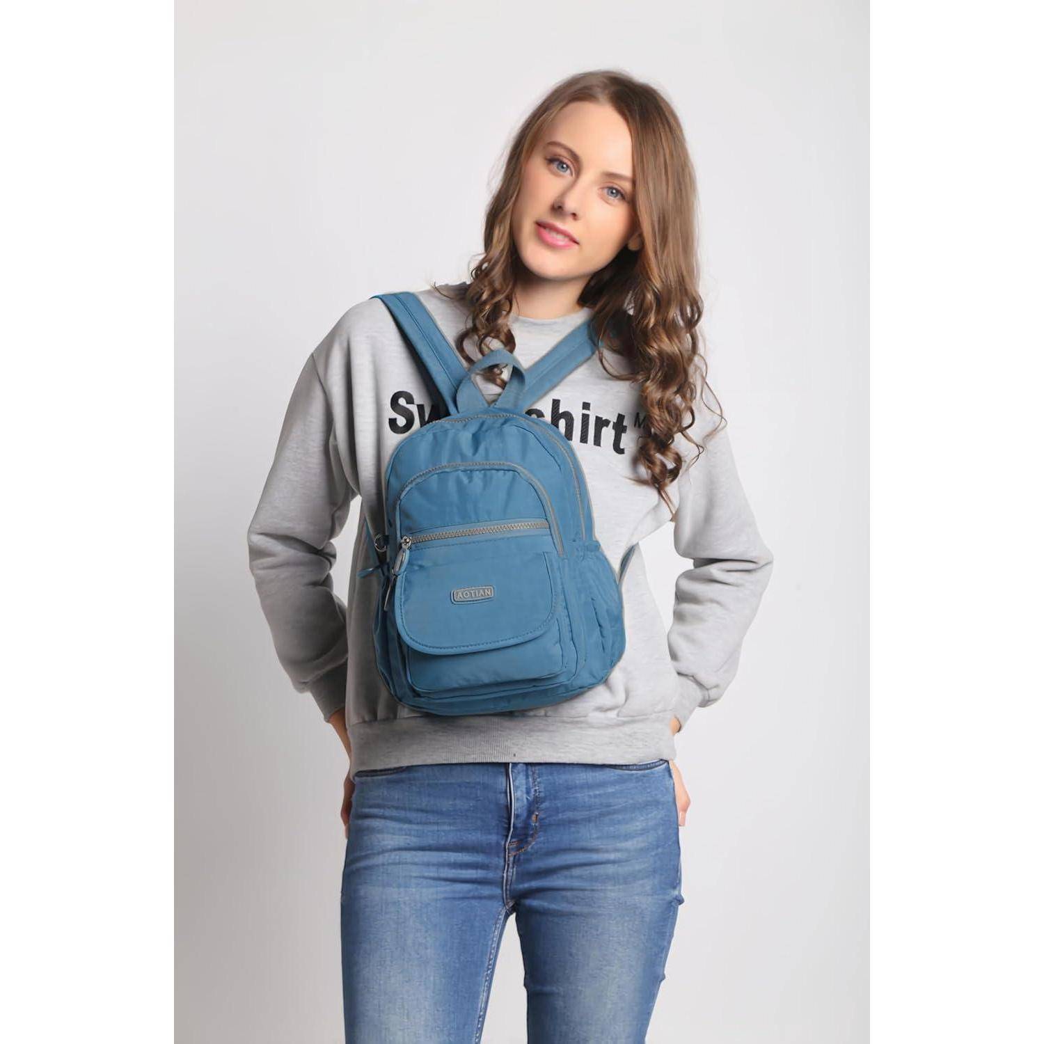 Eine Person mit langen Haaren, die einen grauen Pullover und Jeans trägt, einen blauen Rucksack trägt und eine ruhige, gelassene Miene zeigt.