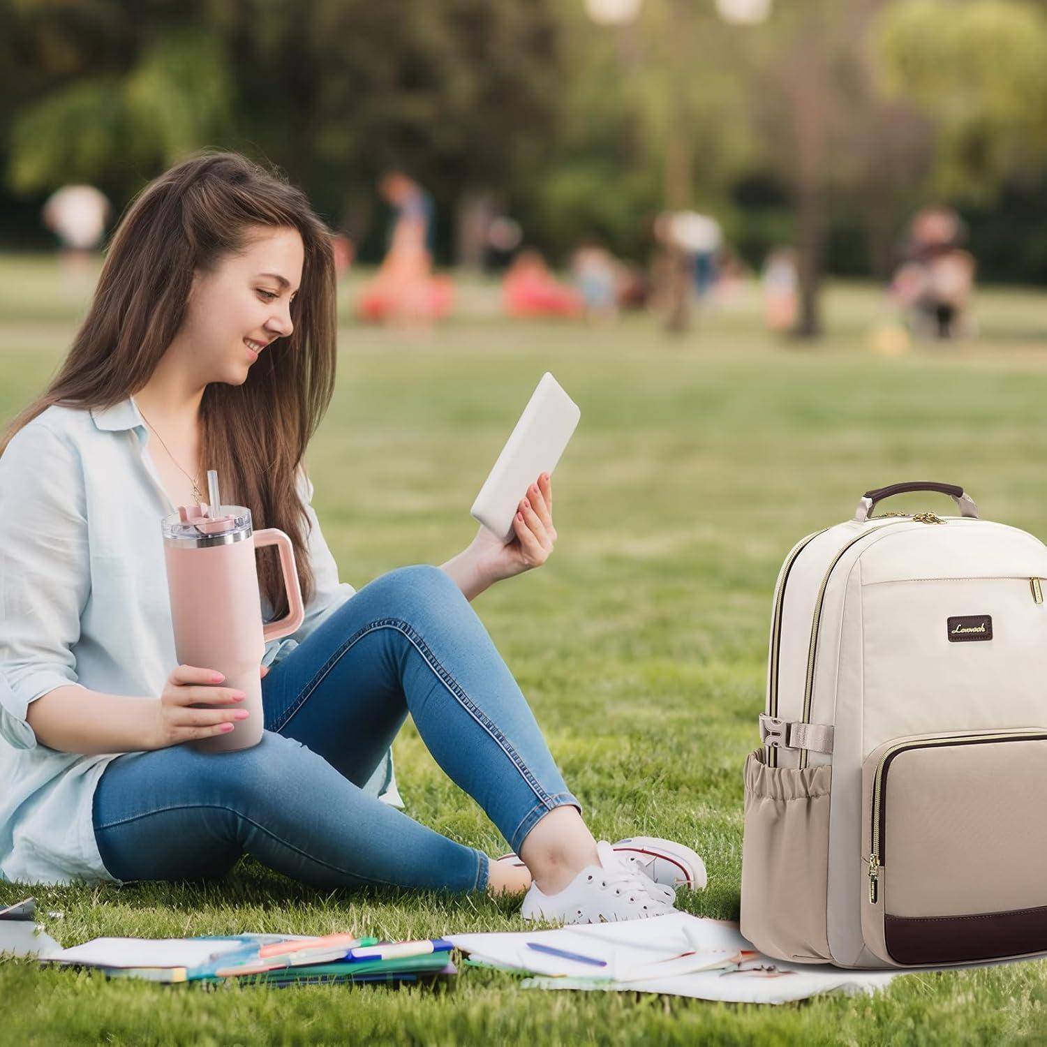 Eine junge Frau sitzt auf dem Gras in einem Park, hält ein Tablet und eine pinke Wasserflasche. Ein Rucksack und Notizbücher liegen neben ihr.