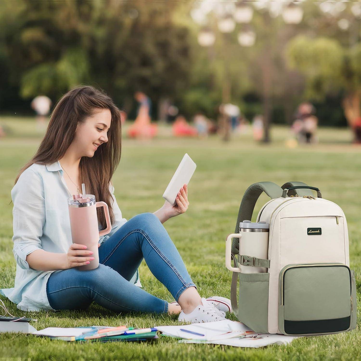 Eine Person sitzt auf Gras in einem Park und hält ein Tablet und eine pinke Flasche. Neben ihr liegt ein grüner Rucksack mit Büchern und einer zweiten Flasche.
