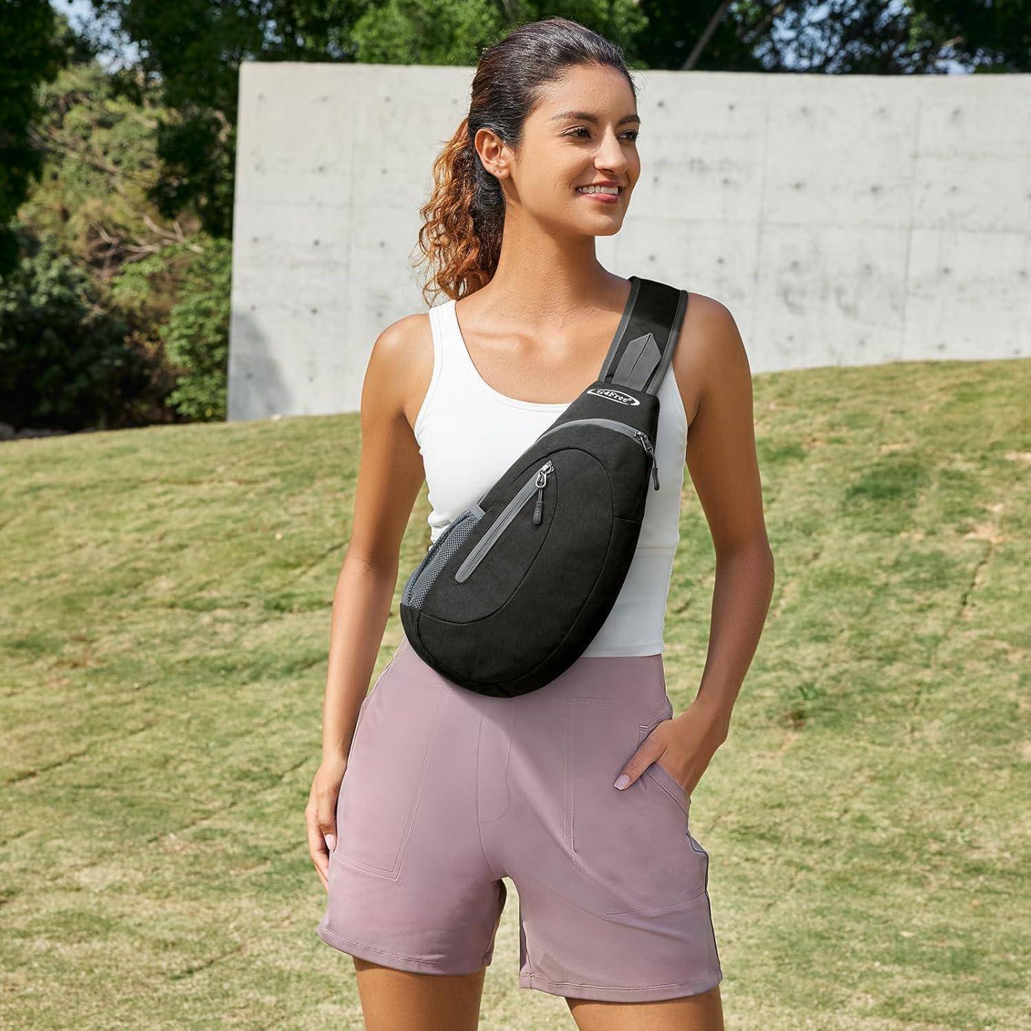 Eine Person mit Pferdeschwanz steht im Freien, trägt ein weißes Trägertop, rosa Shorts und eine schwarze Umhängetasche, lächelt vor einer Wand.