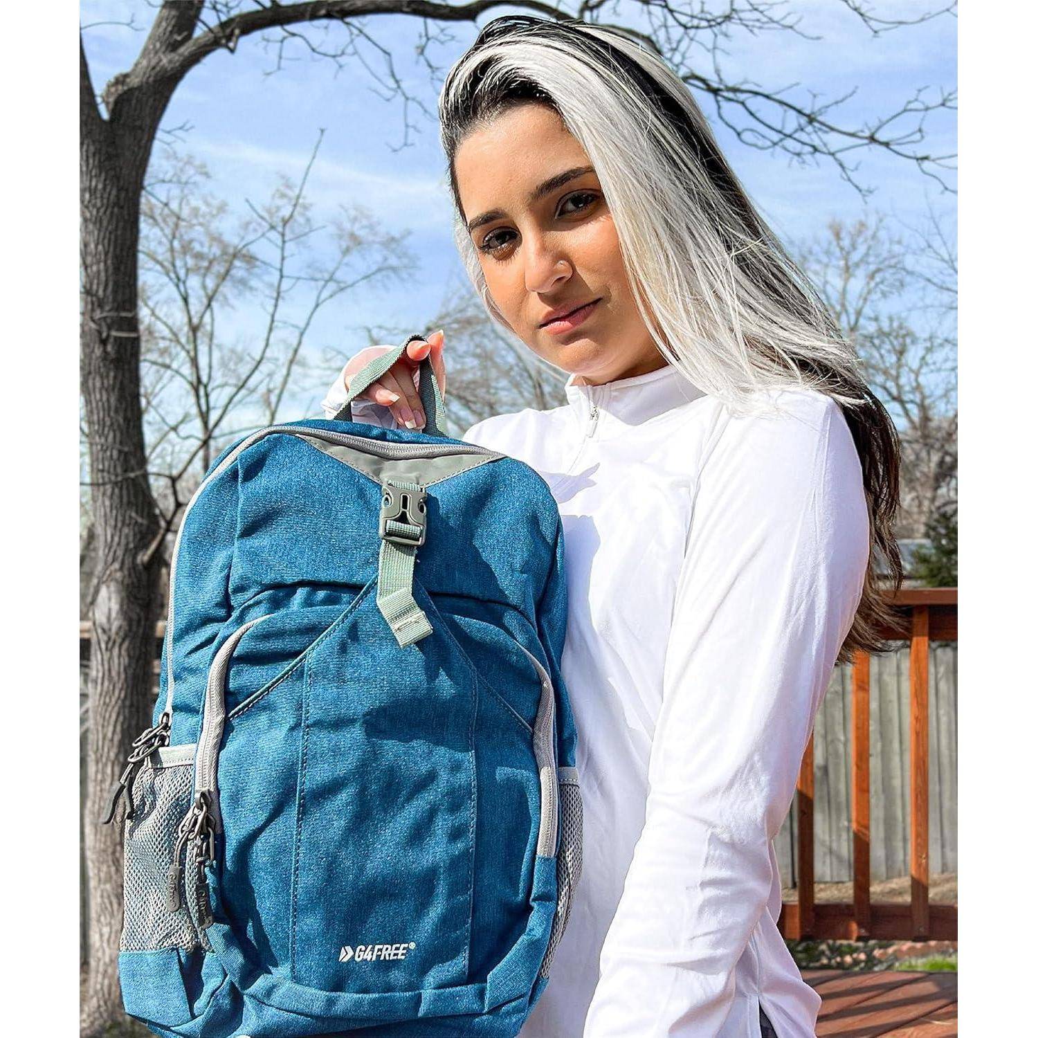 Eine Person mit einem weißen Oberteil steht draußen und hält einen blauen Rucksack mit der Aufschrift 