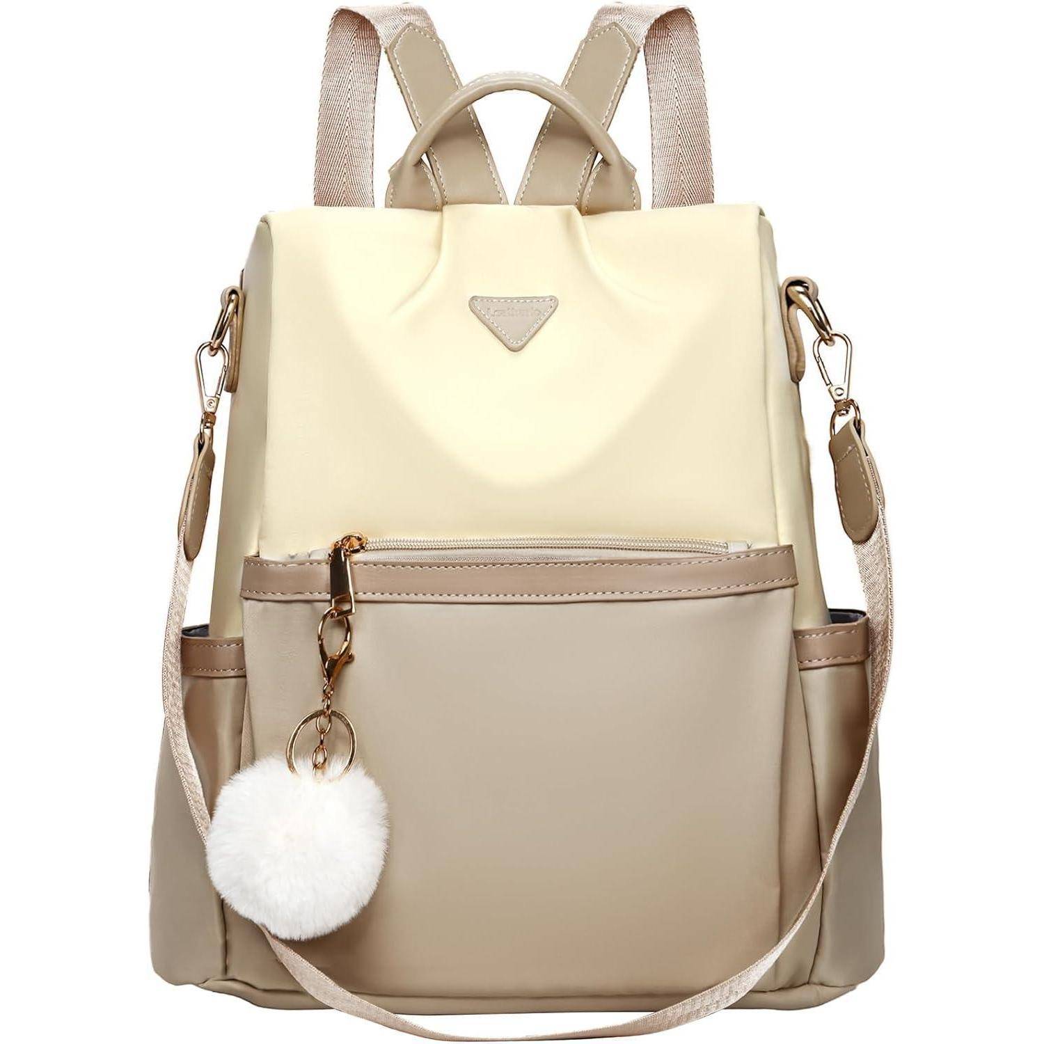 Ein beiger und cremefarbener Rucksack mit einer Fronttasche und einem flauschigen weißen Pompon-Schlüsselanhänger.