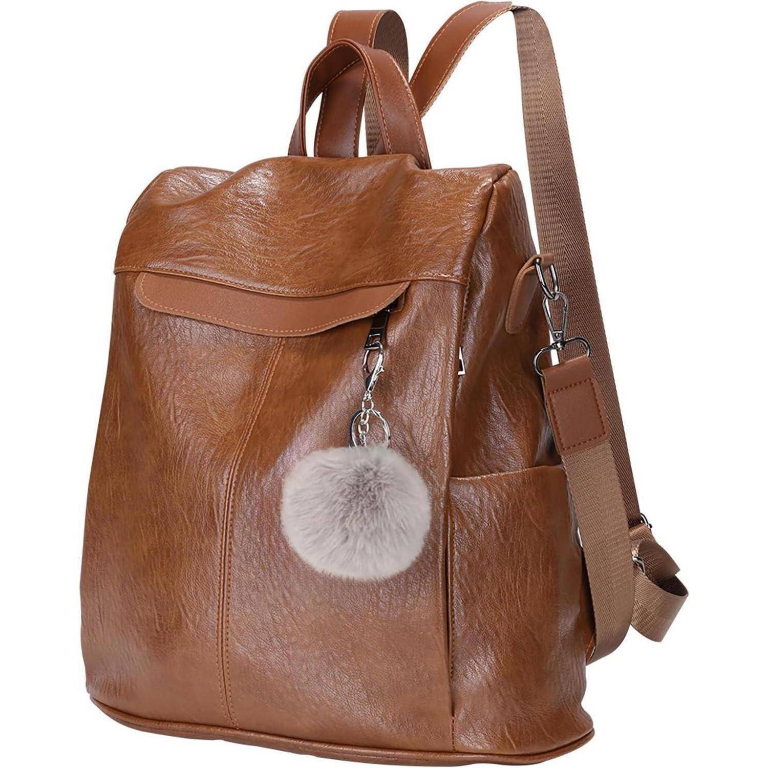 Brauner Lederrucksack mit Tragegriff, verstellbaren Schultergurten und einem flauschigen grauen Pompon-Schlüsselanhänger, der an einem Reißverschluss befestigt ist.