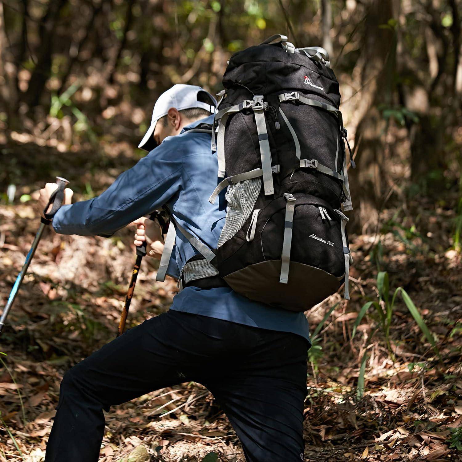 Eine Person, die einen Waldweg entlang wandert, trägt eine blaue Jacke und eine weiße Kappe, hat einen großen schwarzen Rucksack dabei und benutzt Trekkingstöcke.