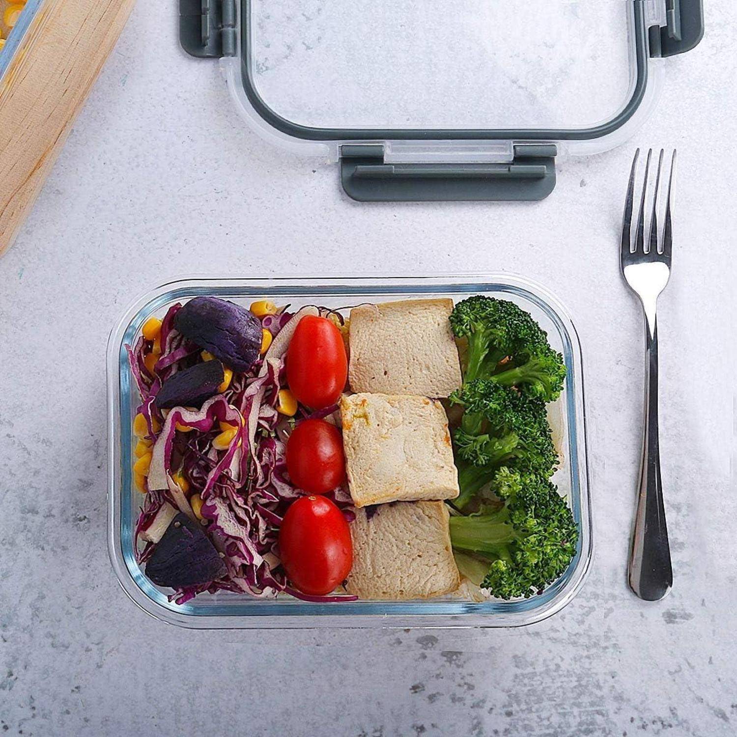 Eine Meal-Prep-Box mit Tofu, Brokkoli, Kirschtomaten, rotem Kohl, Mais und Scheiben von lila Kartoffeln, neben einer Gabel auf einem Tisch platziert.