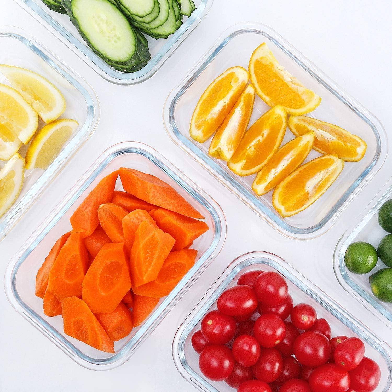 Verschiedene geschnittene Obst- und Gemüsesorten in durchsichtigen Behältern: Gurken, Zitronen, Orangen, Karotten, Kirschtomaten und Limetten auf einer weißen Oberfläche.