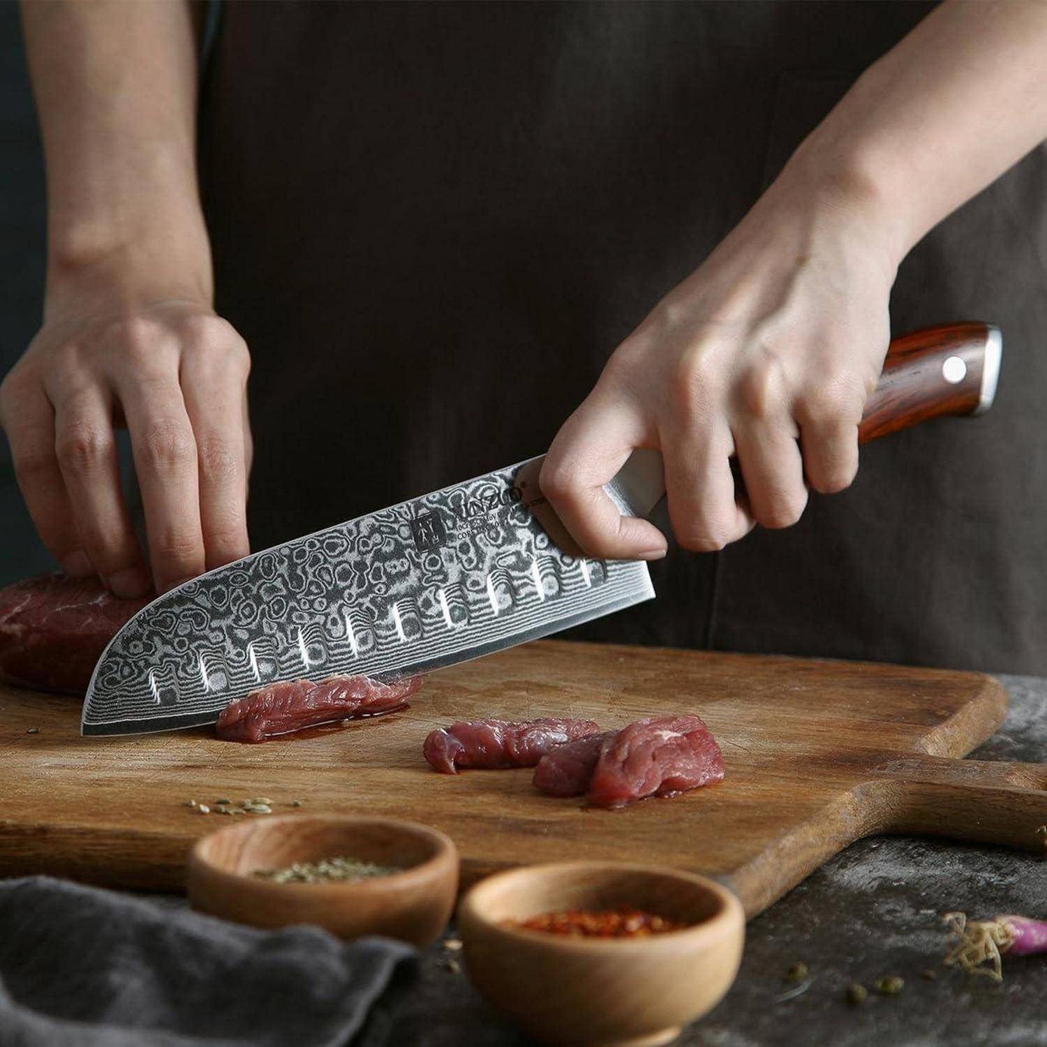 Eine Person, die Fleisch auf einem Holzschneidebrett mit einem dekorativen Kochmesser schneidet. Kleine Schalen mit Gewürzen stehen in der Nähe.