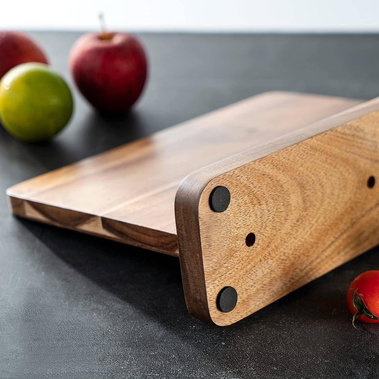 Nahaufnahme eines Holzschneidbretts, das auf der Seite liegt, mit einem Apfel und zwei weiteren Früchten im Hintergrund auf einer Küchenarbeitsplatte.