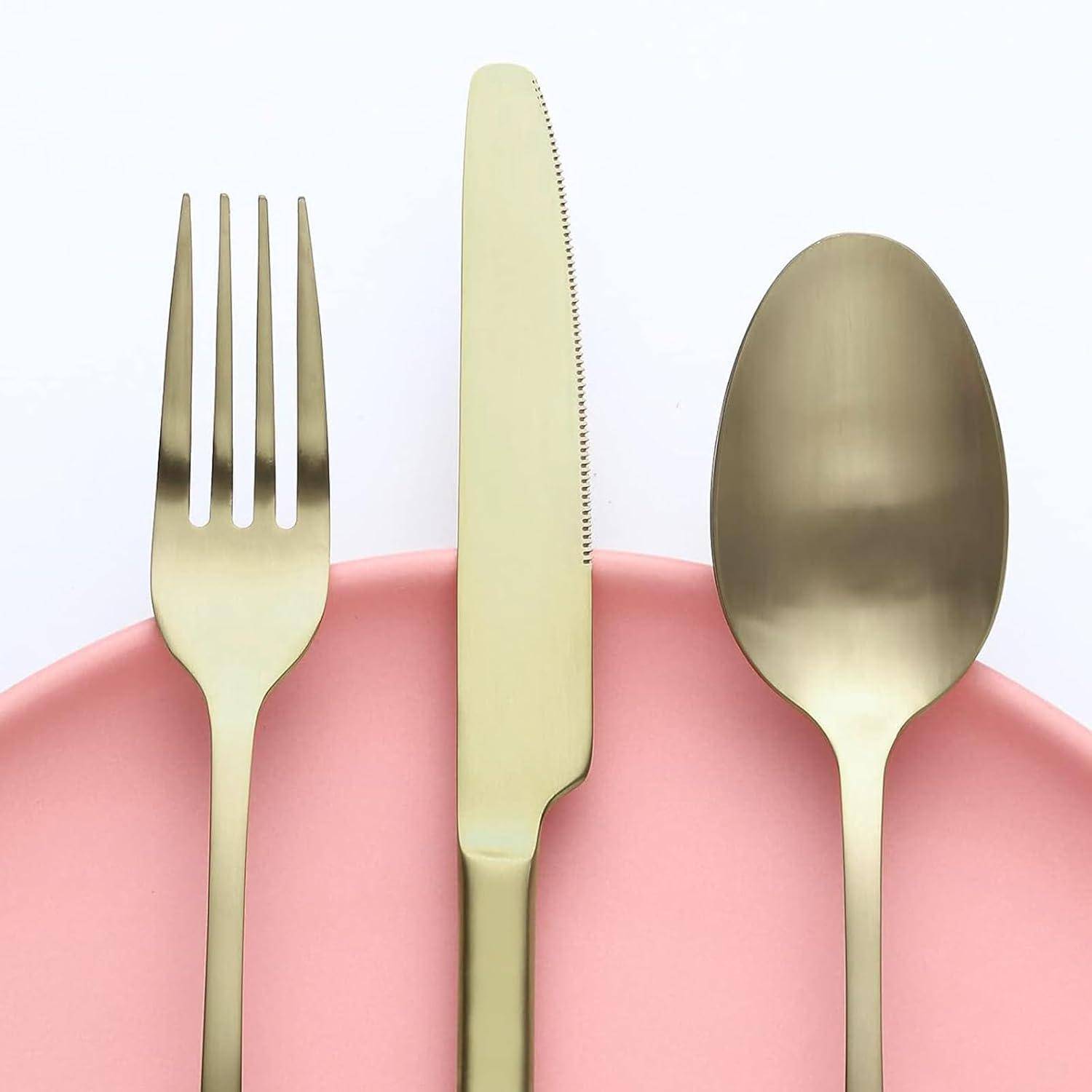 Eine goldene Gabel, ein goldenes Messer und ein goldener Löffel liegen auf einem rosa Teller, in einer formellen Tischgeddeckanordnung platziert.
