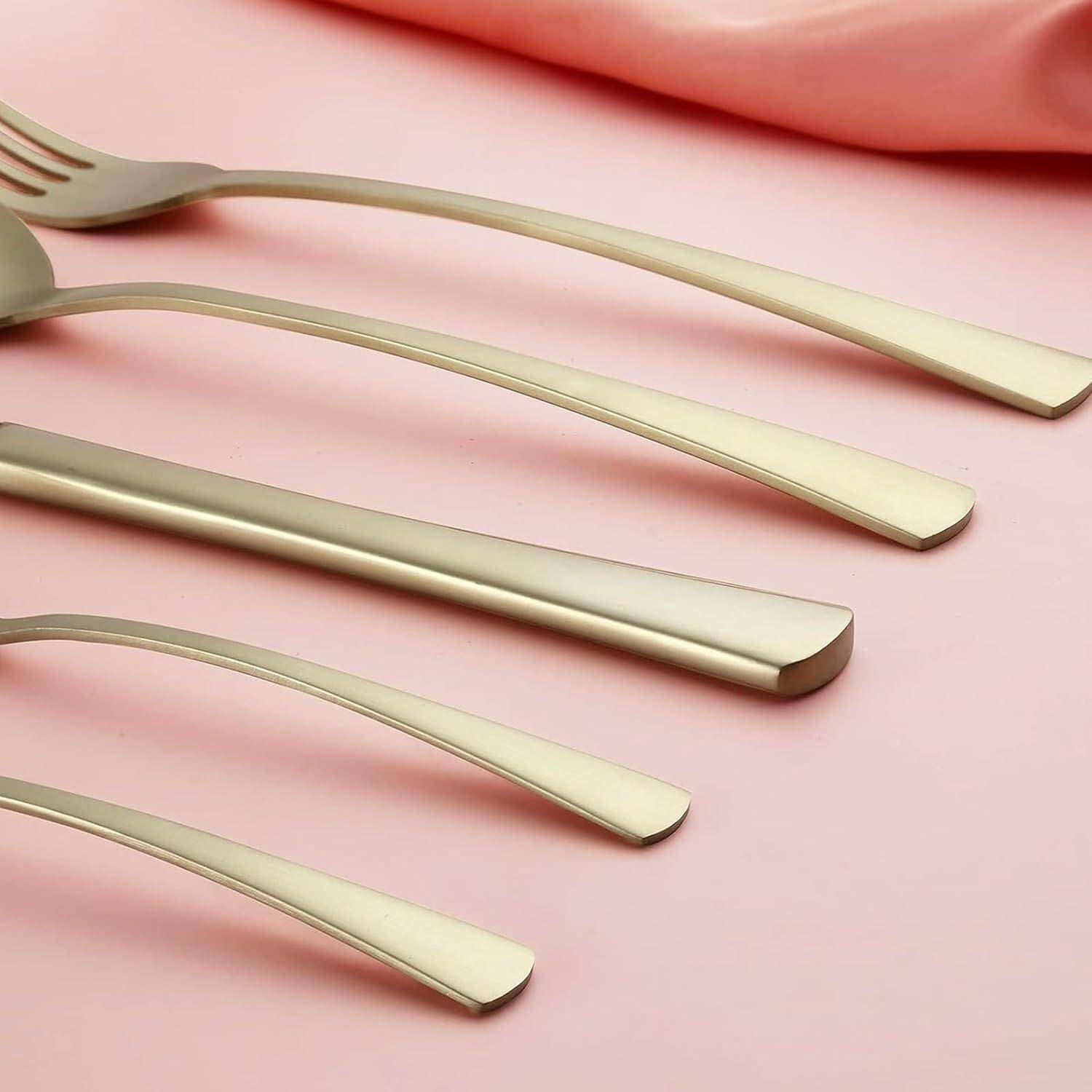 Eine Nahaufnahme eines modernen, geschwungenen Besteck-Sets auf einer blassrosa Oberfläche, die eine Gabel, ein Messer und einen Löffel mit schlanker metallischer Finish zeigt.