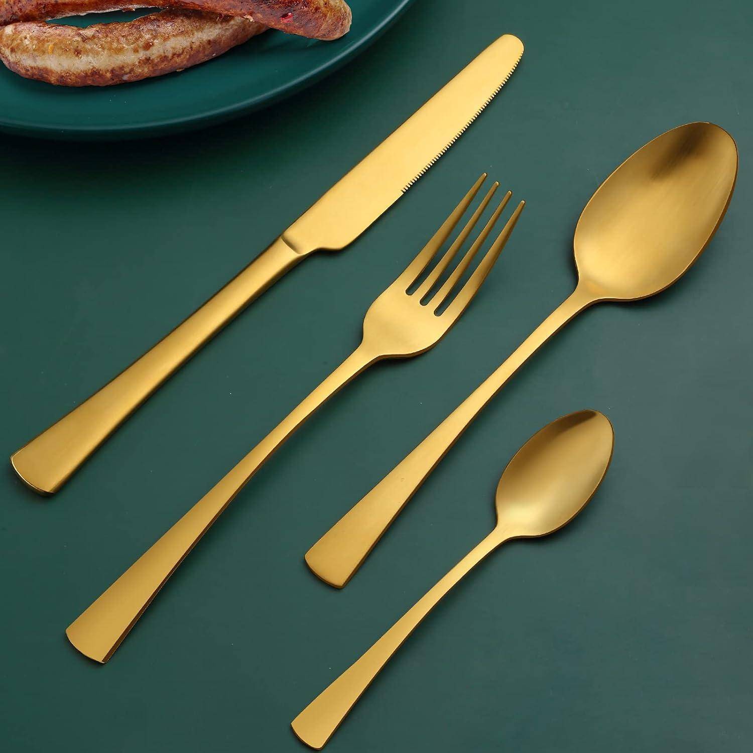 Goldenes Besteckset mit einem Buttermesser, einer Gabel und zwei Löffeln auf einer grünen Oberfläche neben einem Teller mit Würstchen.