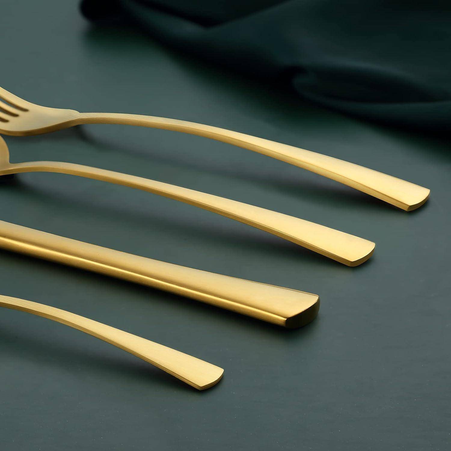 Ein Set aus elegantem goldenem Besteck, bestehend aus einer Gabel, einem Messer, einem Löffel und einem Dessertlöffel, ordentlich auf einer dunklen Oberfläche angeordnet.