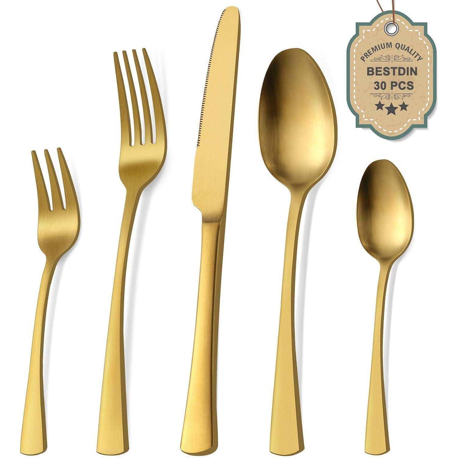 Goldenes Besteckset, das eine Gabel, ein Messer, einen Löffel, eine Dessertgabel und einen Teelöffel umfasst. Ein Etikett trägt die Aufschrift 
