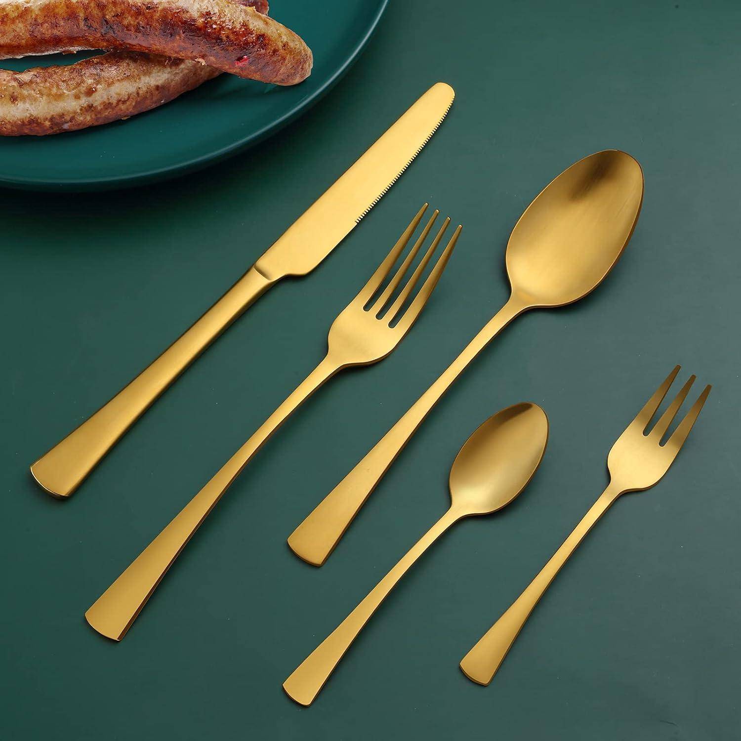 Goldenes Besteckset mit einem Messer, einer Gabel und Löffeln, die auf einem grünen Tisch neben einem Teller mit knusprigem Brot angeordnet sind.