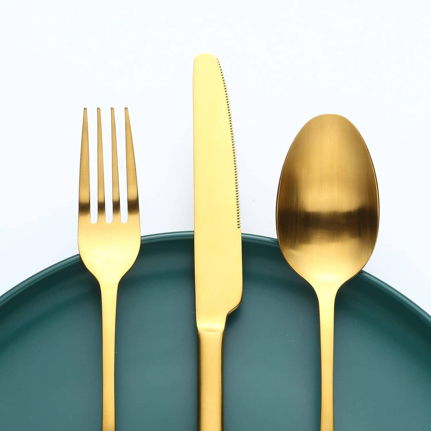 Eine goldene Gabel, ein Messer und ein Löffel sind sorgfältig auf einem dunkelgrünen Teller vor einem schlichten weißen Hintergrund angeordnet, was Eleganz und Dining andeutet.