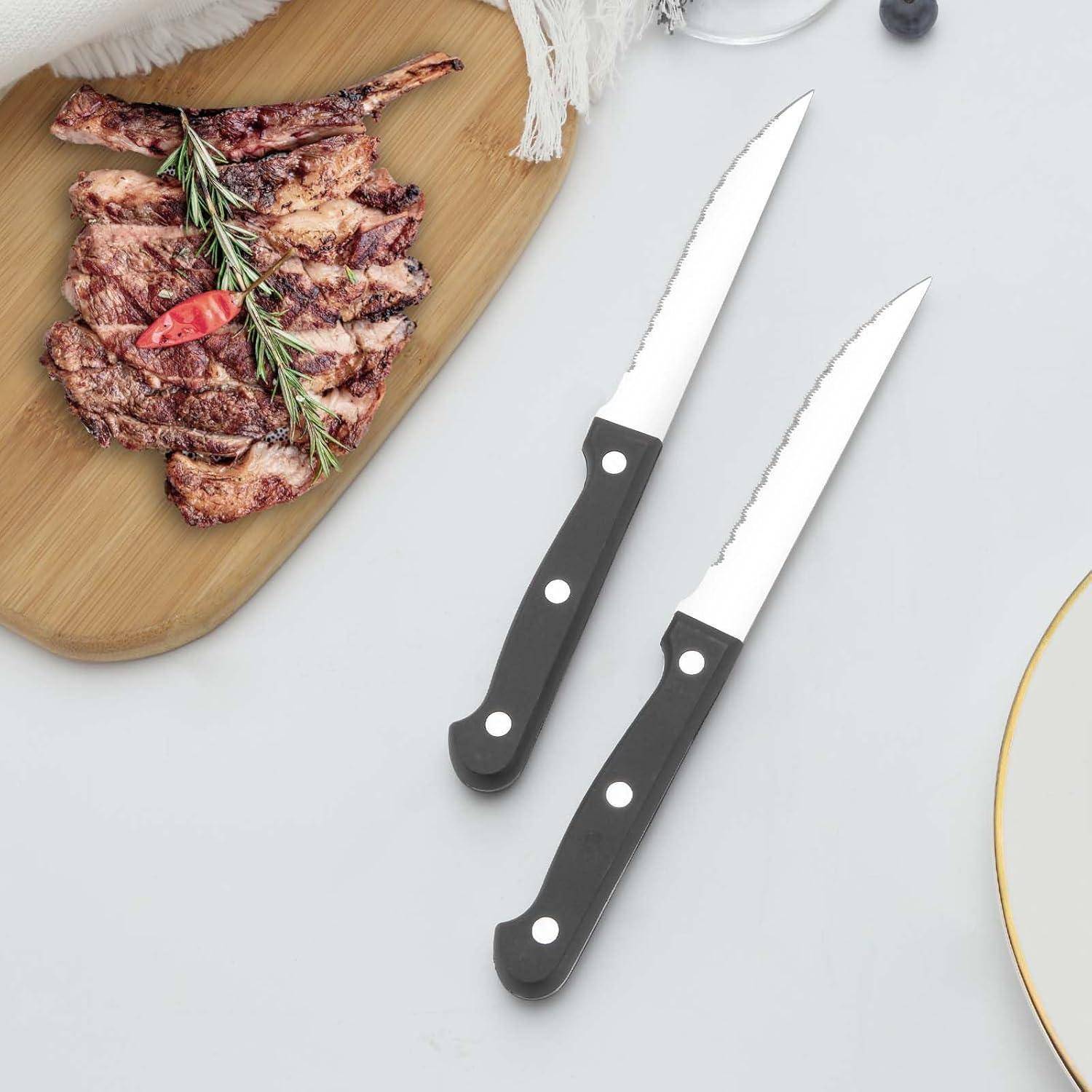 Gegrillte Lammkoteletts mit Rosmarin und einer roten Chilischote auf einem Holzbrett; zwei schwarzgriffige Steakmesser liegen daneben.