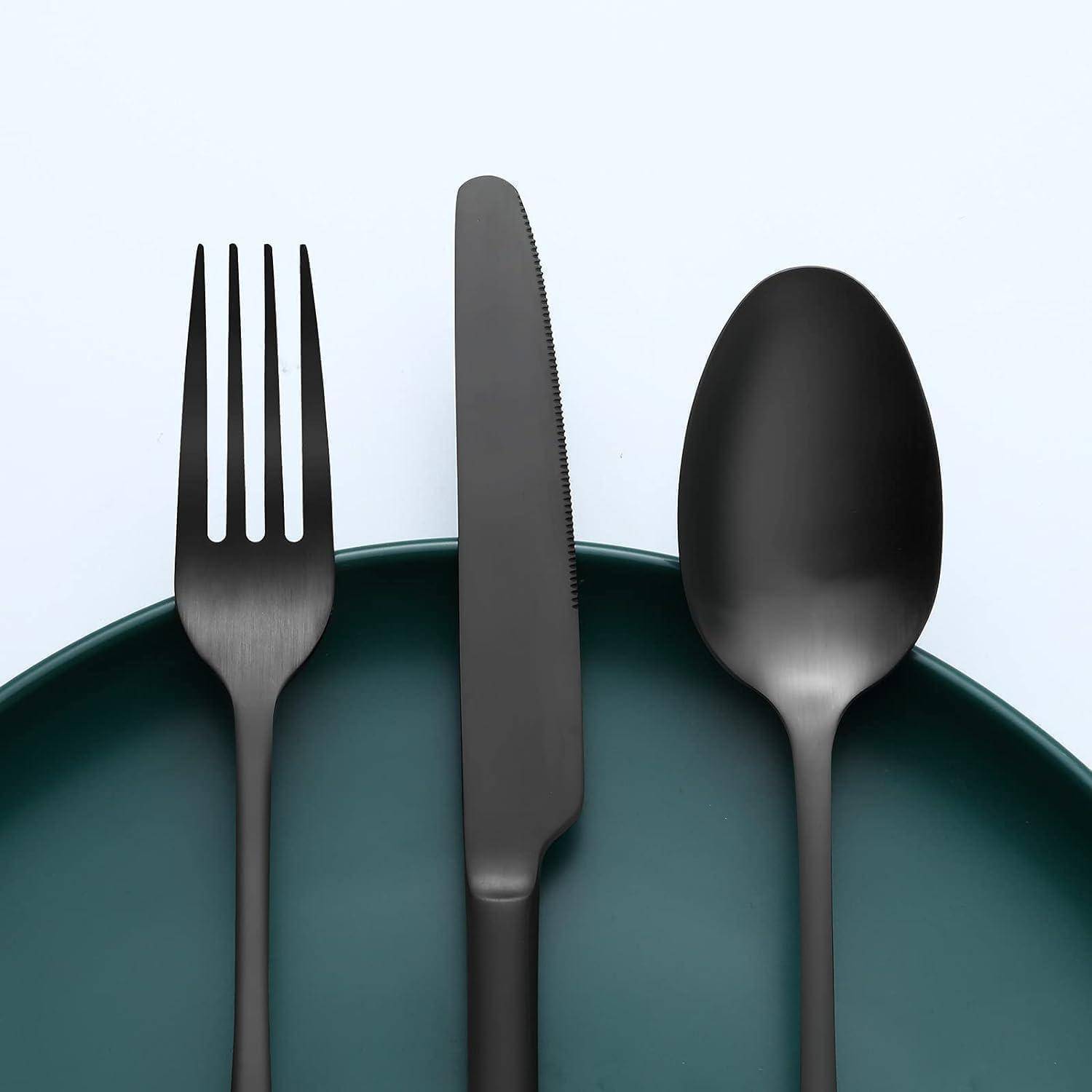 Ein Set an schwarzen matten Besteck, bestehend aus Gabel, Messer und Löffel, die auf einem dunkelgrünen Teller angeordnet sind und eine minimalistische Tischgedekung kreieren.