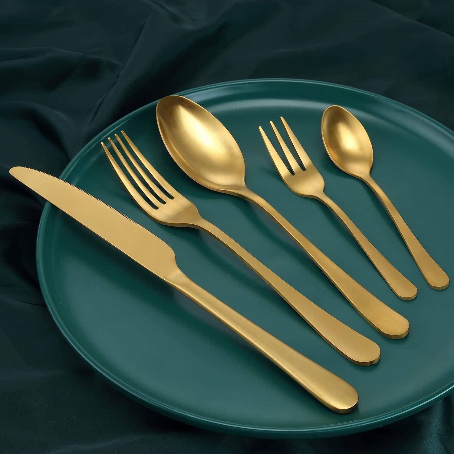 Ein grüner Teller trägt ein passendes goldenes Besteck-Set: ein Messer, eine Gabel, einen großen Löffel, einen kleinen Löffel und eine Dessertgabel, ordentlich angeordnet.
