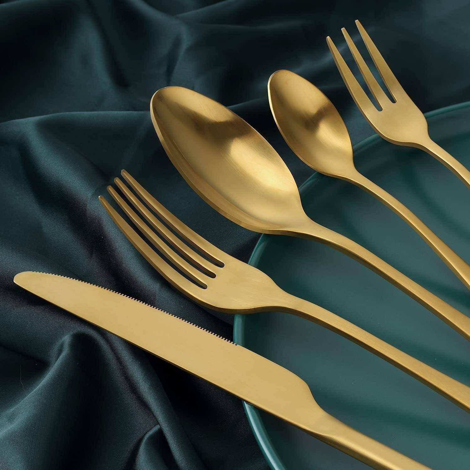 Goldene Gabel, Messer, Löffel und Teelöffel, auf einem dunkelgrünen Seidenstoff angeordnet, die eine luxuriöse und elegante Tischgeddeckung schaffen.