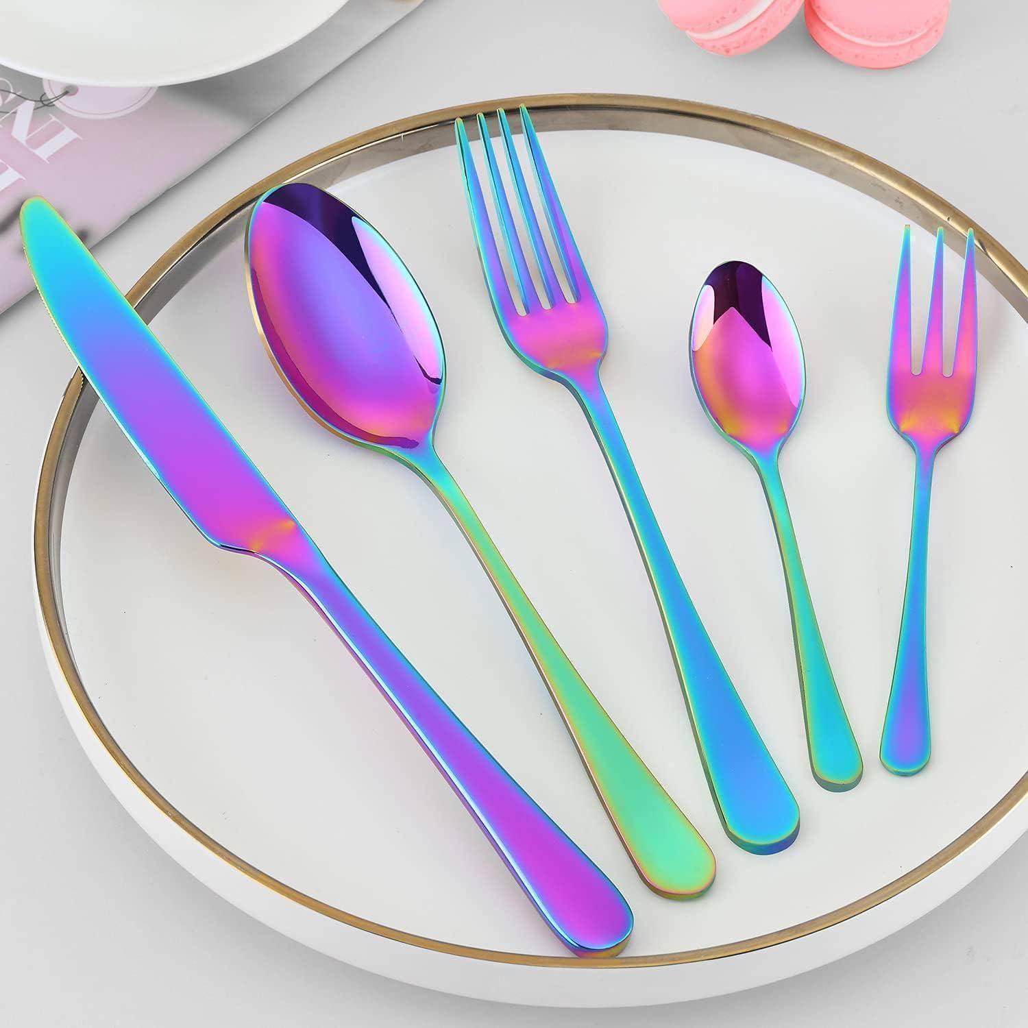 Ein Set Regenbogen-farbener Bestecke, bestehend aus einem Messer, einem großen Löffel, einer Gabel, einem kleinen Löffel und einer Dessertgabel, die auf einem weißen Teller angeordnet sind.