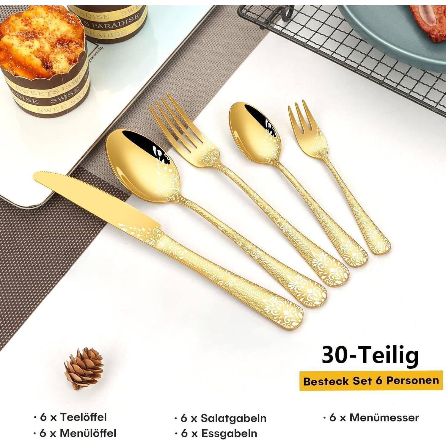 Goldenes Besteck-Set mit kunstvollen Griffen, bestehend aus je 6 Messern, Gabeln, Löffeln, Dessertgabeln und Teelöffeln. Ein Cupcake steht auf dem Tisch in der Nähe.