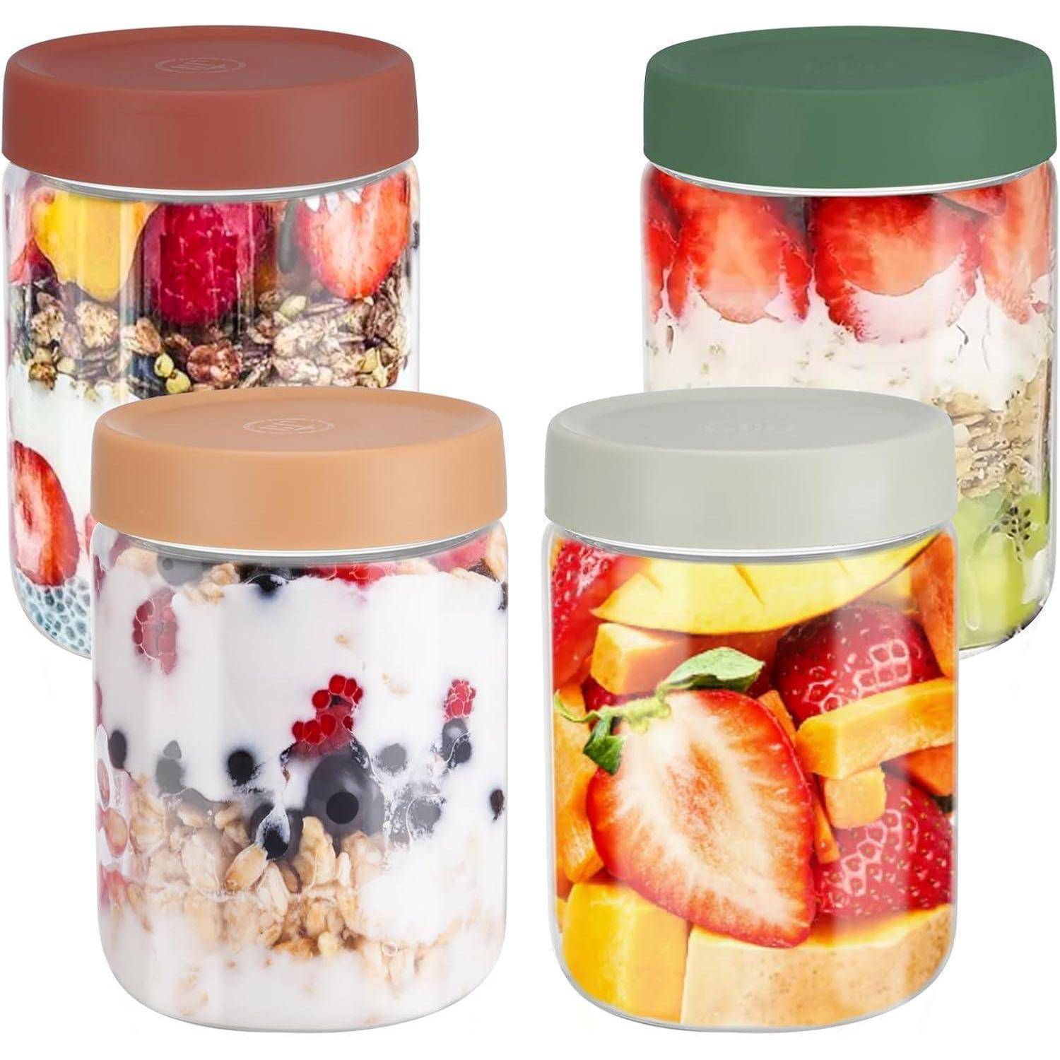 Vier durchsichtige Gläser, gefüllt mit farbenfrohen Schichten aus Früchten, Joghurt und Müsli, jedes mit einem anders gefärbten Deckel versehen.