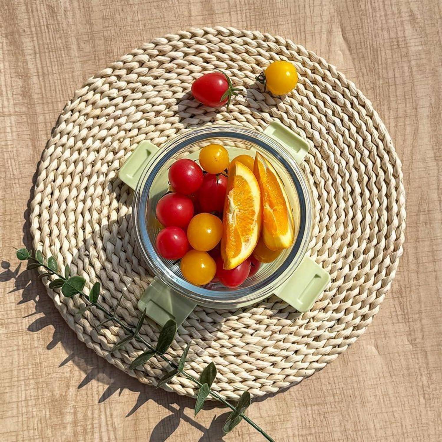Eine Schüssel mit roten und gelben Kirschtomaten und Orangenscheiben, die auf einem geflochtenen Platzdeckchen platziert ist. Ein paar Tomaten liegen neben der Schüssel.