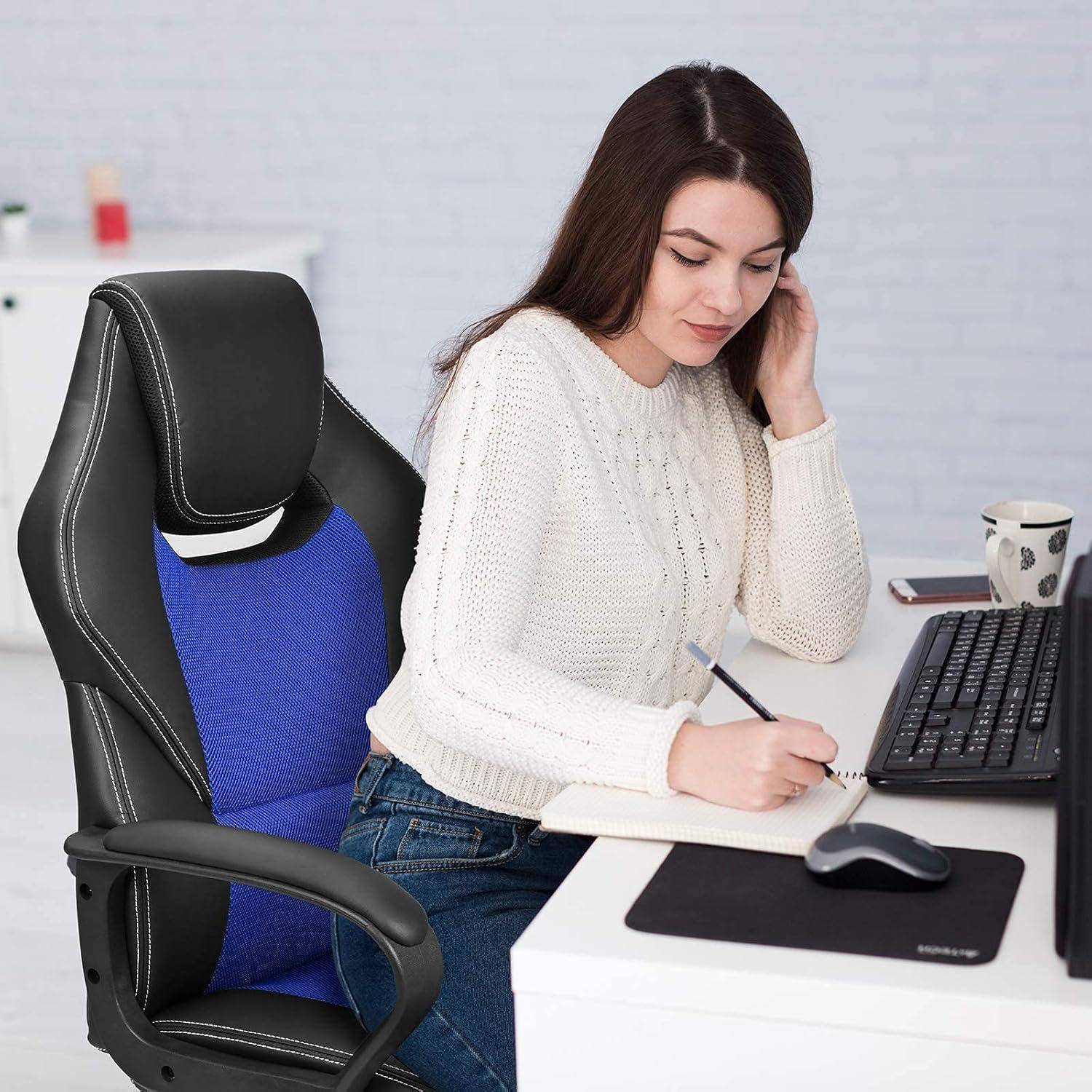 Eine Frau sitzt an einem Schreibtisch, schreibt Notizen und blickt dabei auf einen Computerbildschirm. Auf dem Schreibtisch steht eine Tasse, und der Stuhl hat einen blauen Sitzbezug.