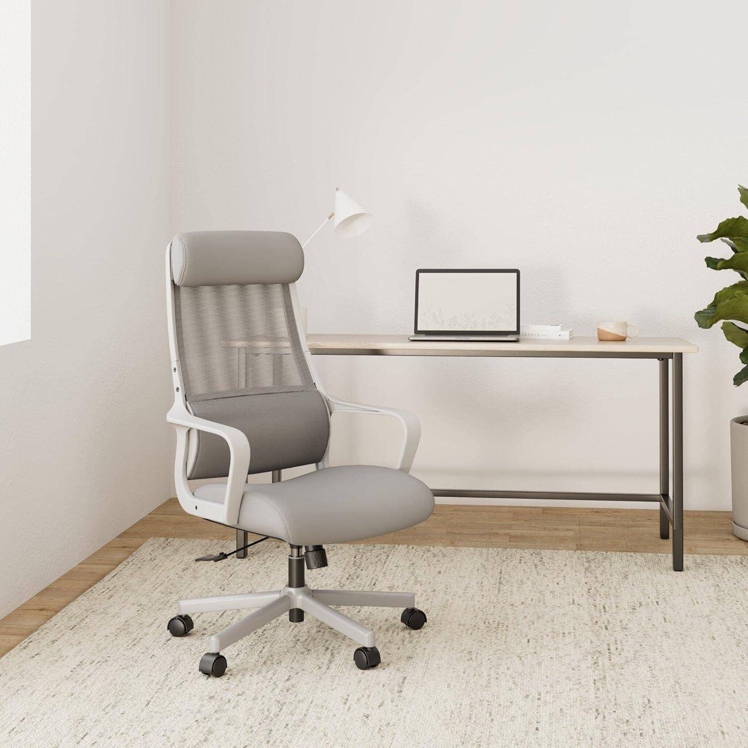 Ein moderner Büroarbeitsplatz mit einem grauen Drehstuhl, einem minimalistischen Schreibtisch mit einer Lampe, einer Pflanze und dekorativen Gegenständen vor einer weißen Wand.