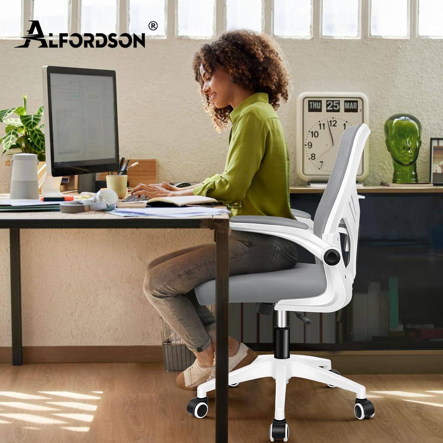 Eine Person, die an einem Computer an einem Schreibtisch in einem Home Office arbeitet und auf einem weißen ergonomischen Stuhl sitzt, neben einem großen Fenster mit natürlichem Licht.