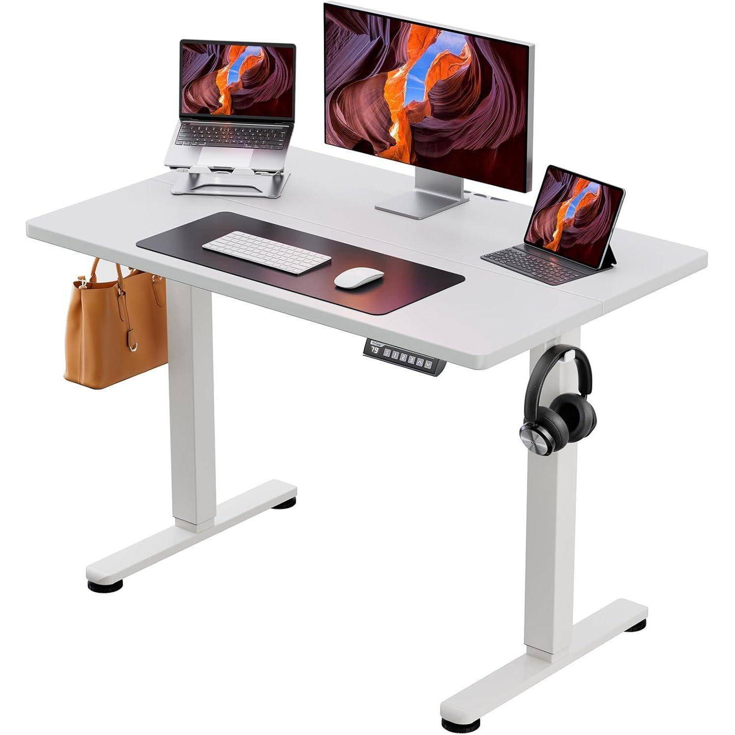 Ein weißer Stehschreibtisch mit einem Monitor, Laptop und Tablet zeigt lebendige abstrakte Designs. Eine Tastatur, Maus, Kopfhörer und eine Handtasche hängen in der Nähe.