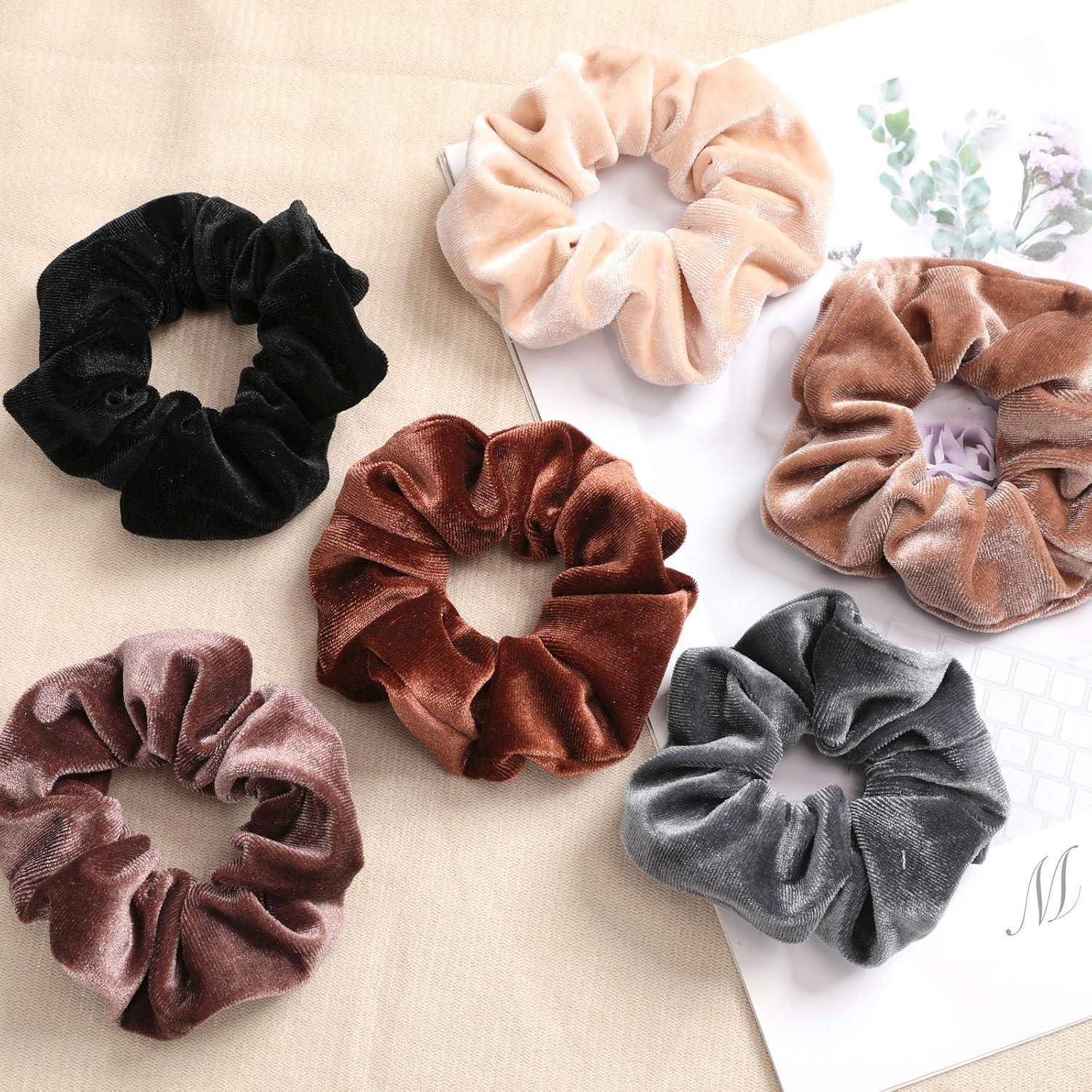 Fünf Haargummis aus Samt in den Farben Schwarz, Beige, Braun, Bordeauxrot und Grau sind in einem Kreis auf einem Tisch neben einem Blumenpapier angeordnet.