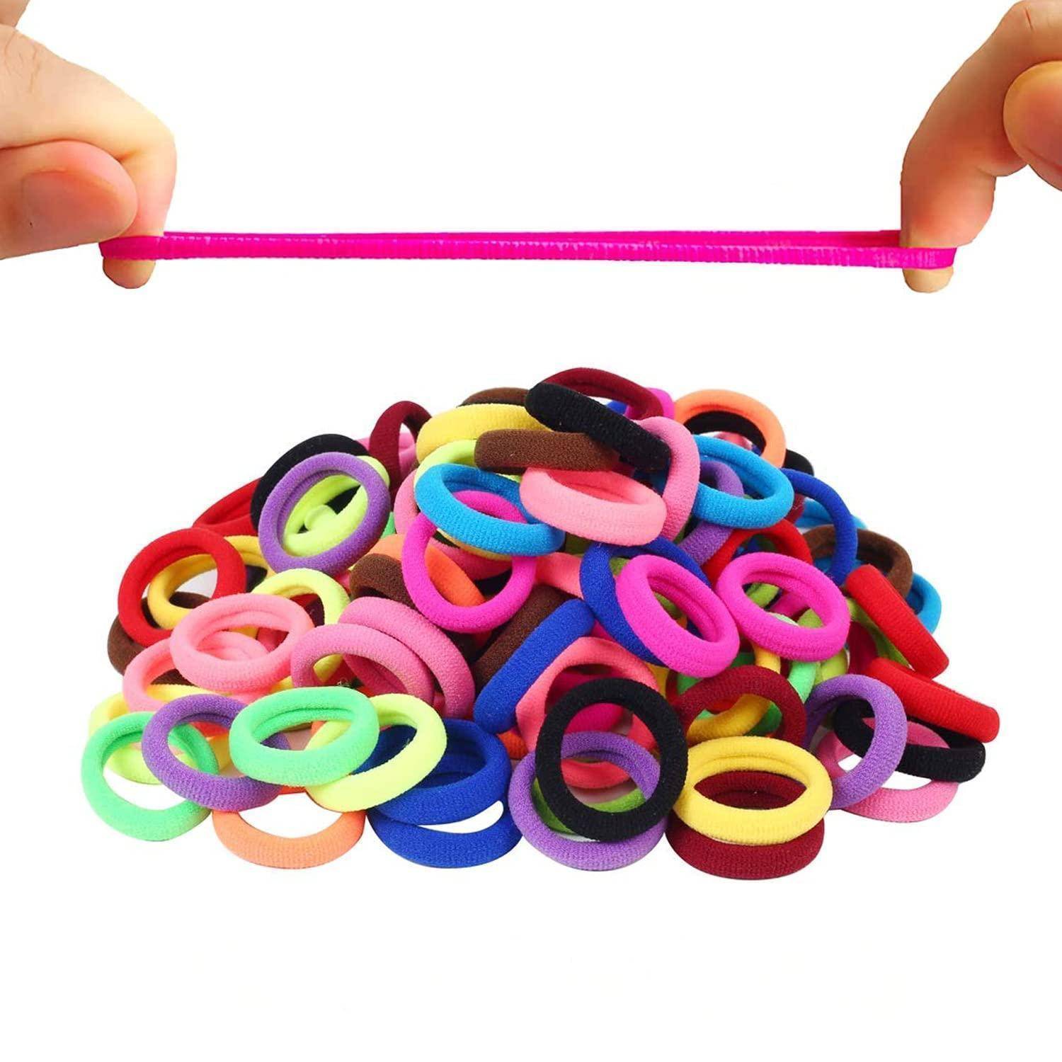 Zwei Hände spannen ein rosafarbenes elastisches Haargummi über einen Haufen von mehrfarbigen Haargummis.