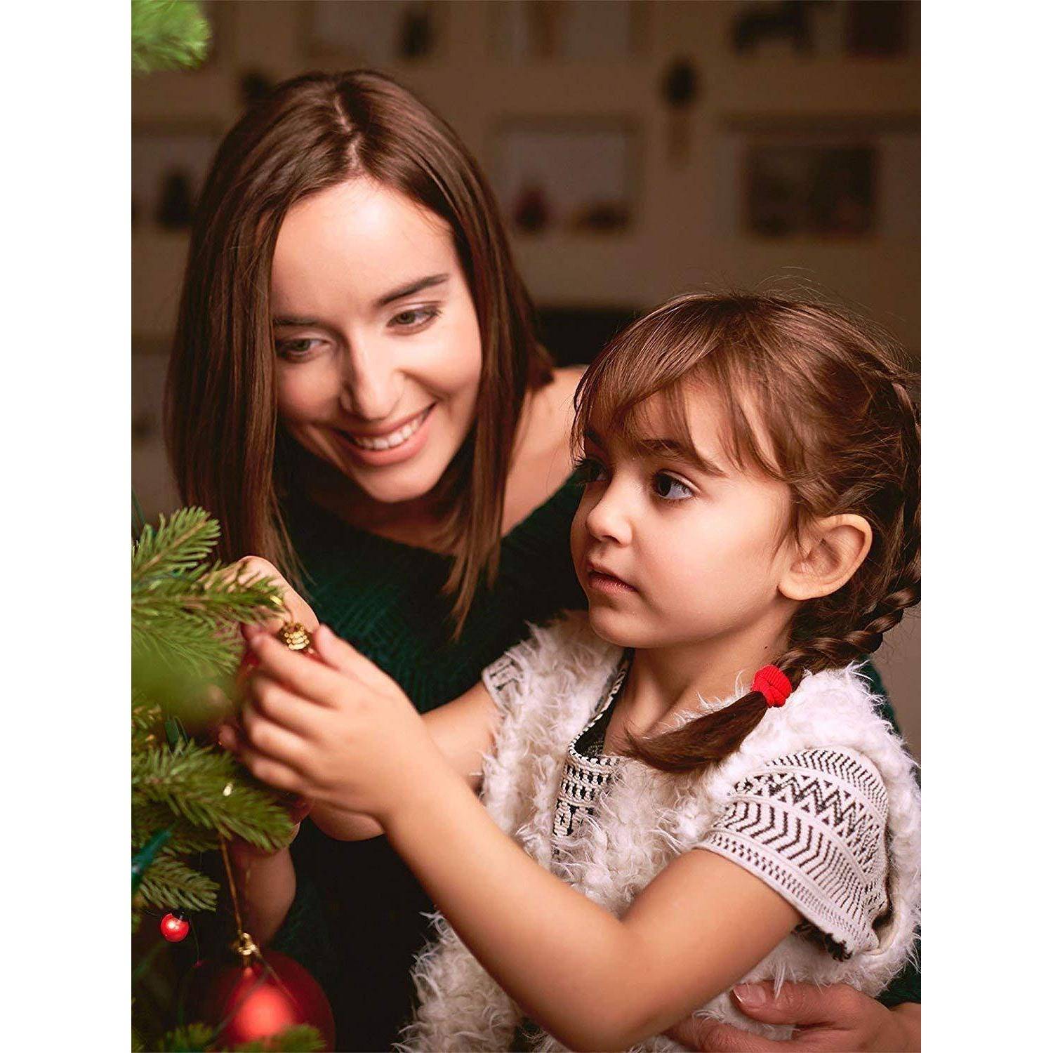 Eine Frau und ein junges Mädchen schmücken gemeinsam einen Weihnachtsbaum und hängen Christbaumkugeln an die Zweige. Sie wirken fröhlich und konzentriert.
