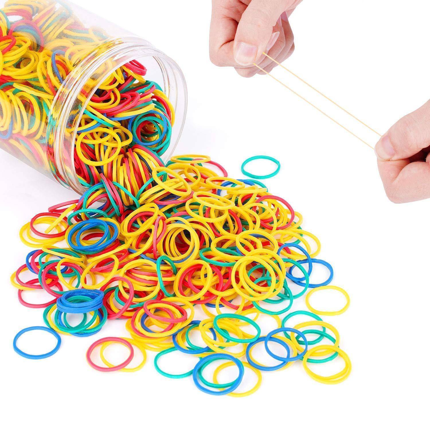 Ein Behälter verschüttet farbenfrohe Gummibänder - rot, blau, gelb, grün - auf eine Oberfläche. Eine Hand streckt ein Gummiband nach oben.