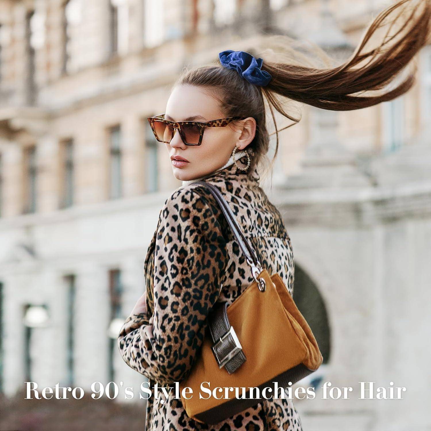 Eine Frau mit Sonnenbrille und Leopardenmantel steht draußen, ihr Haar weht im Wind, zusammengehalten von einem blauen Scrunchie. Text lautet: 